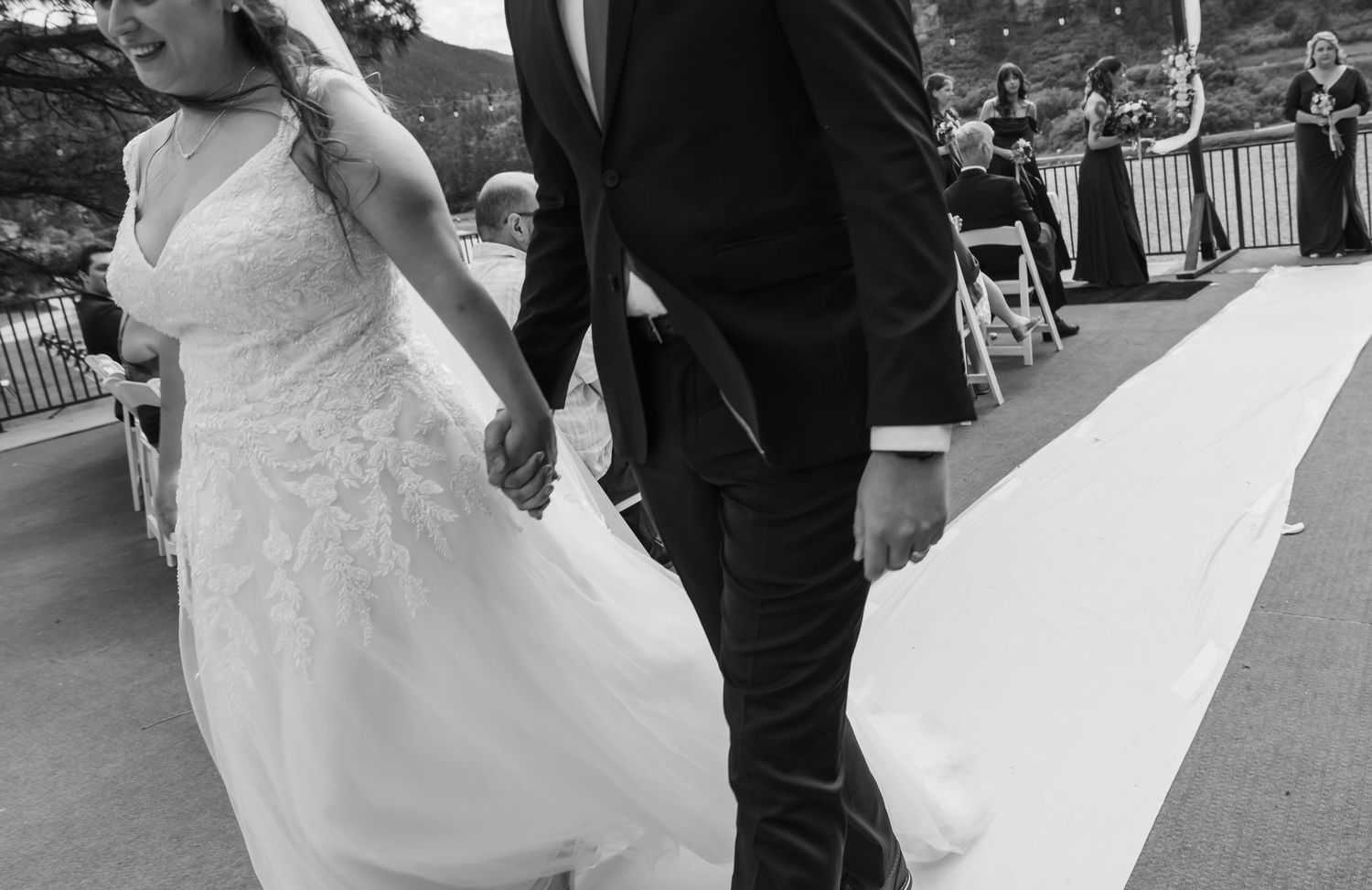 A black and white capture of newlyweds walking together at their outdoor reception.