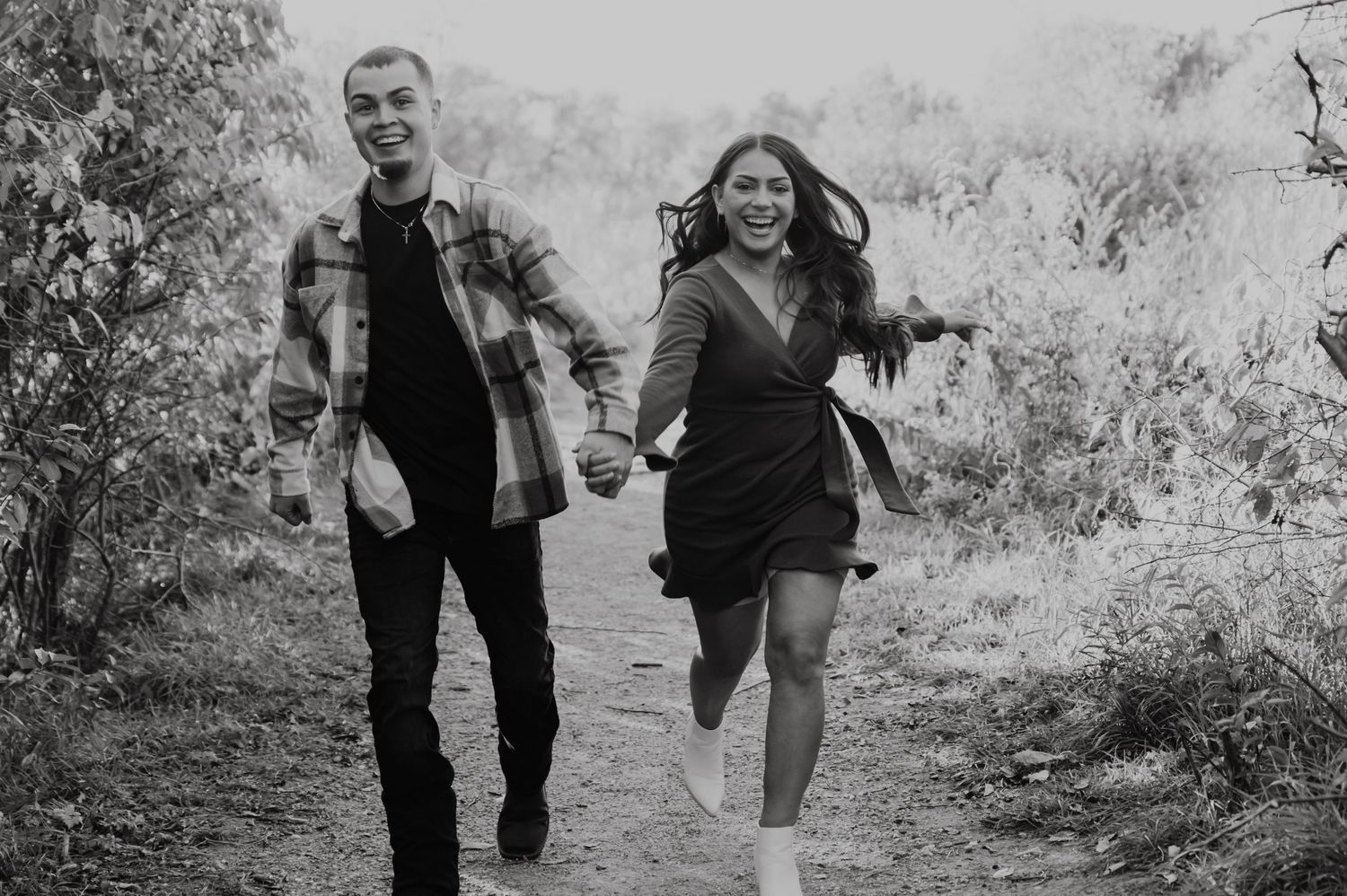 A couple runs joyfully together on a nature trail in black and white.