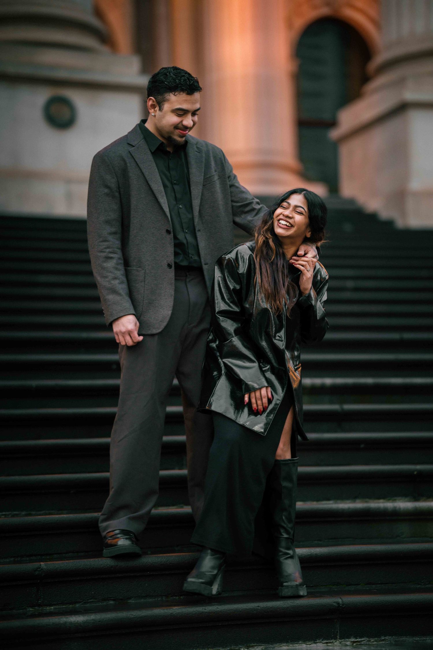 Laughing couple descending grand stone steps of a historic building at twilight.