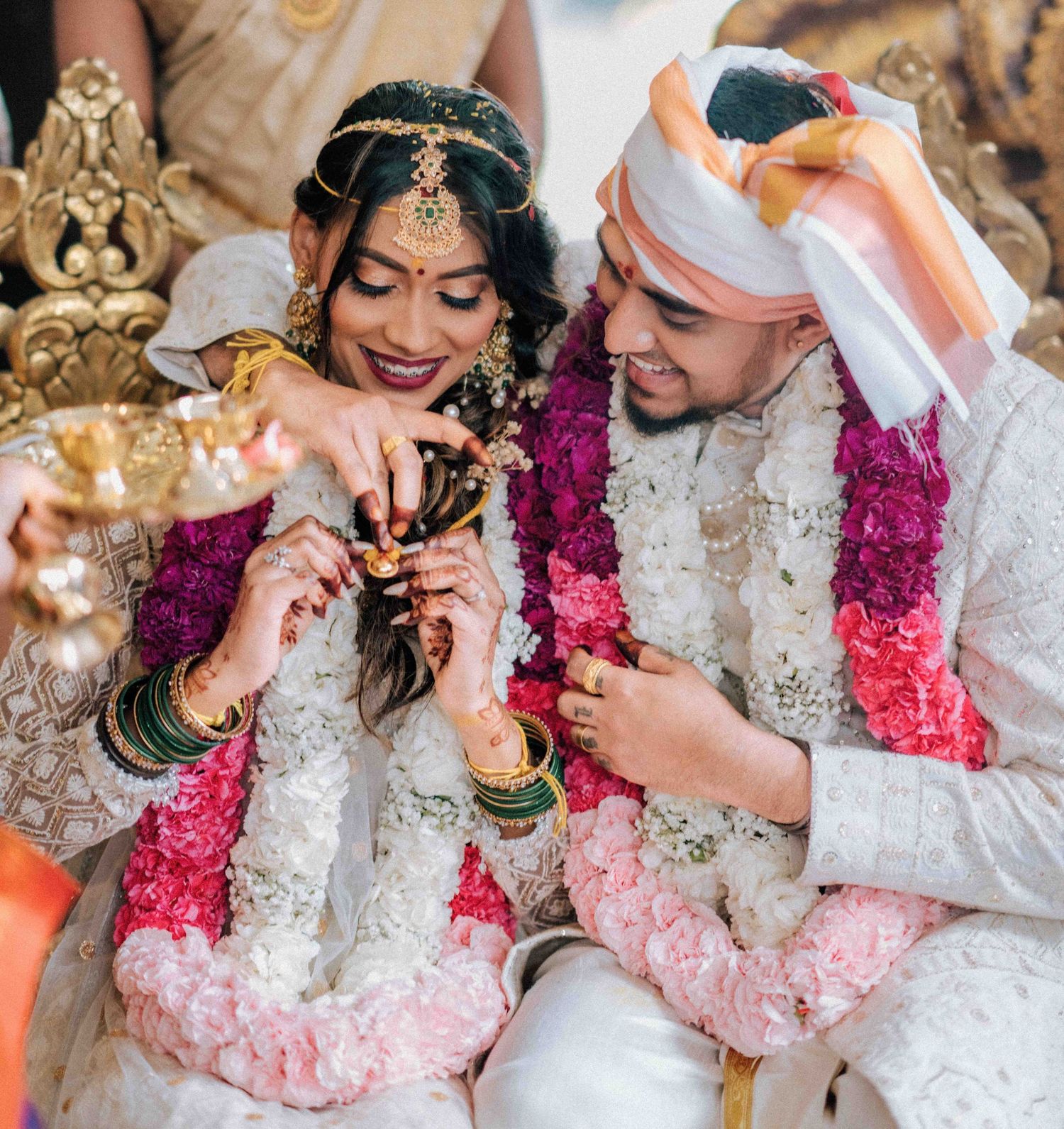 Indian bride and groom in traditional wedding attire exchanging rings during Hindu ceremony with floral garlands.