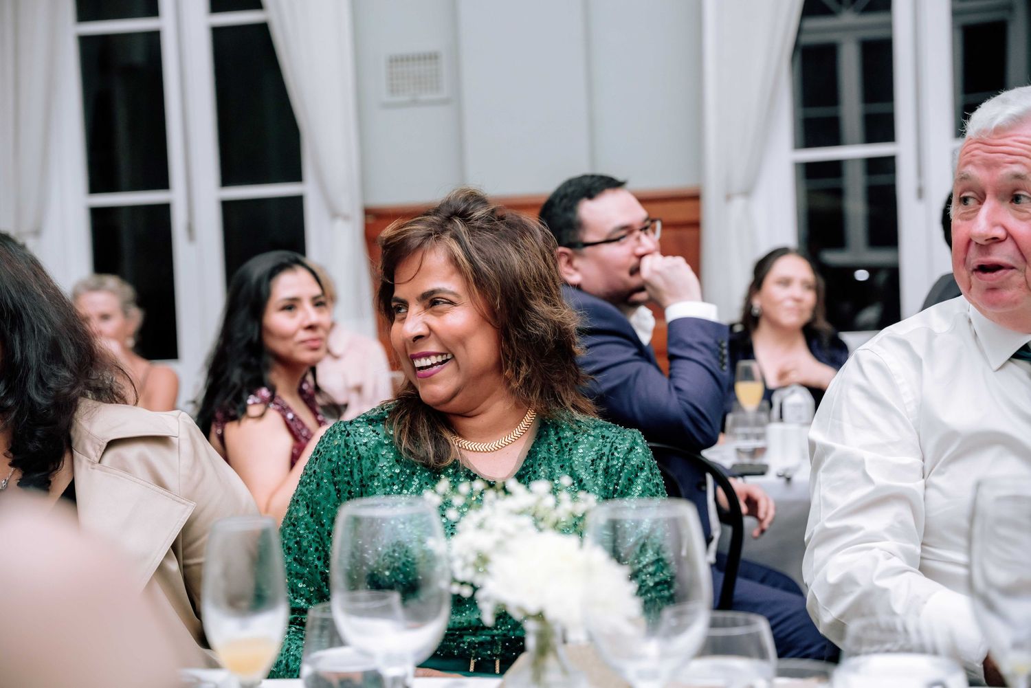 Smiling woman in green dress enjoys laughter with other guests at festive wedding reception dinner.