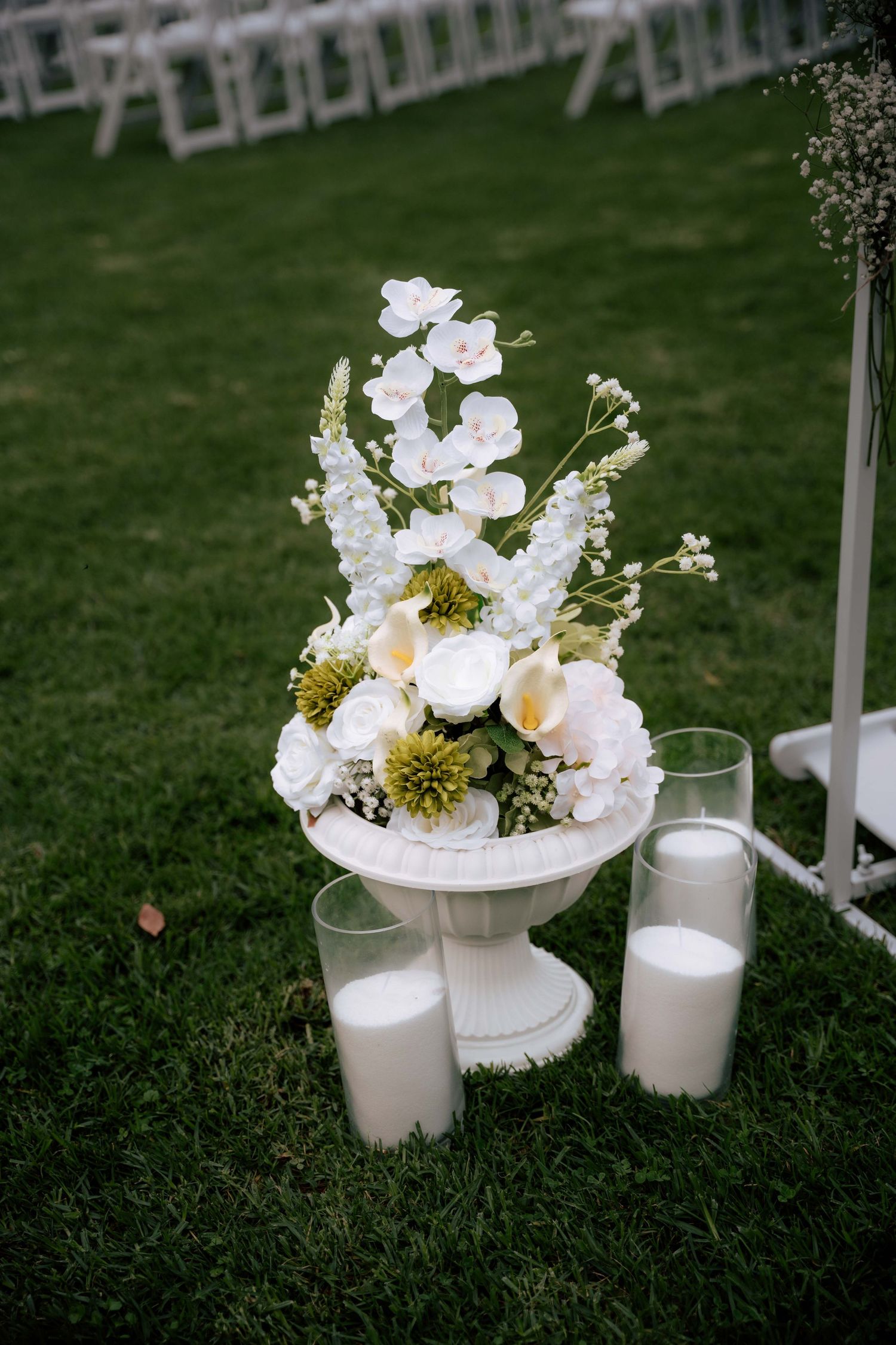 White floral arrangement with orchids and candles decorating outdoor wedding ceremony.