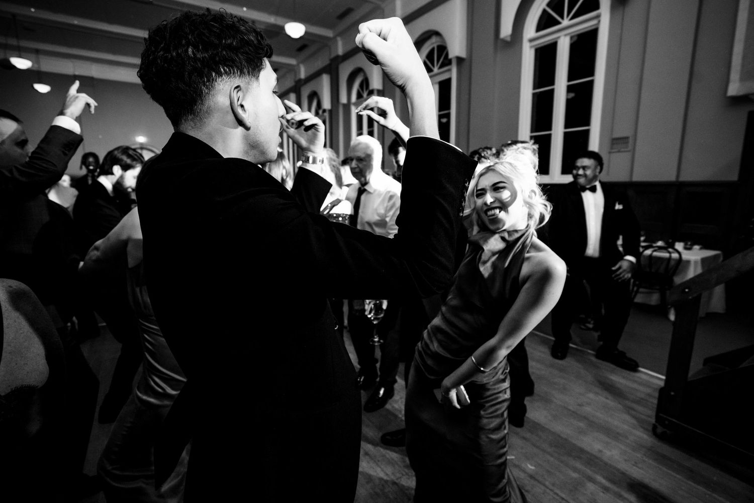 Black and white photo of guests dancing joyfully at lively wedding reception celebration.