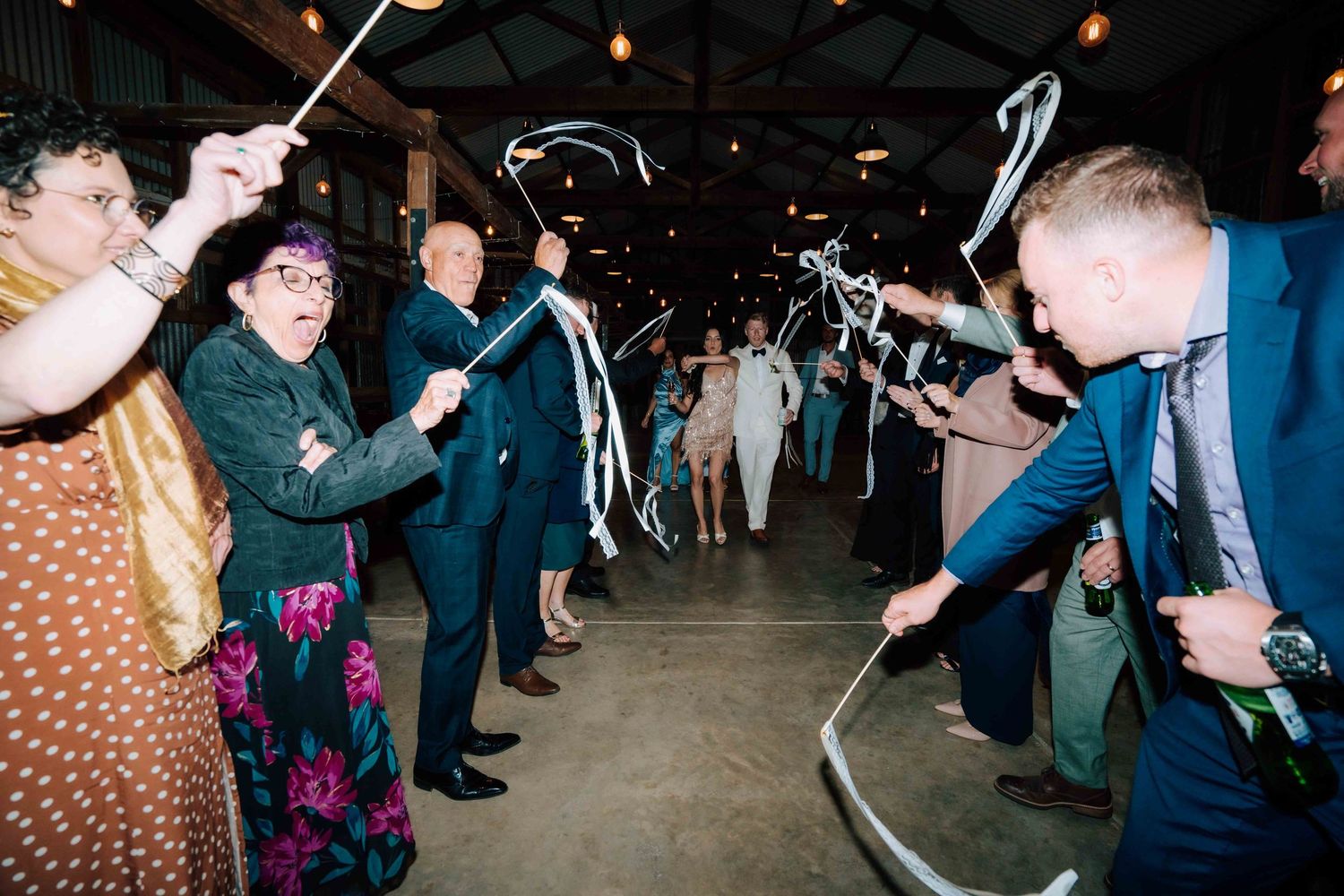 Wedding guests celebrate with sparklers and streamers during a lively send-off at an indoor evening reception.