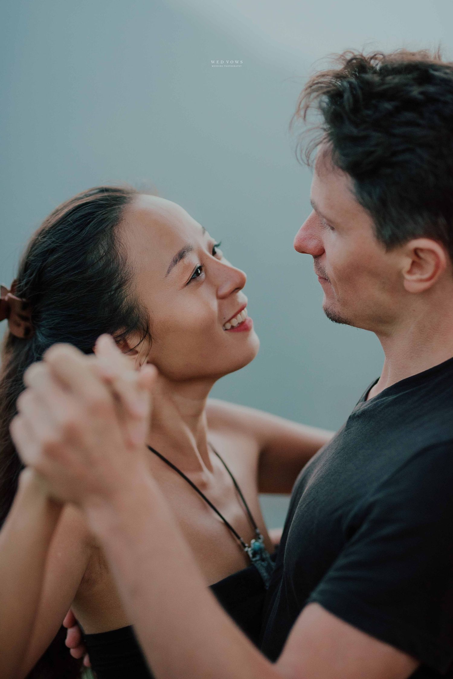A happy interracial couple dancing together, smiling and gazing into each others eyes romantically.