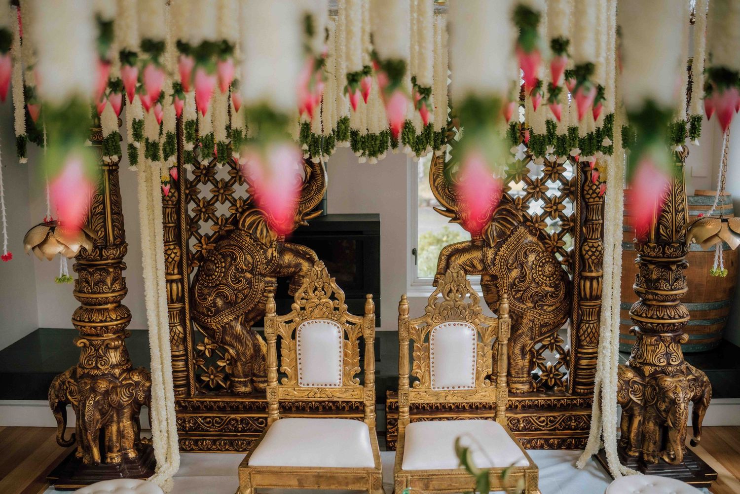 Ornate golden mandap chairs decorated with elephant carvings and pink floral hangings for Hindu wedding.
