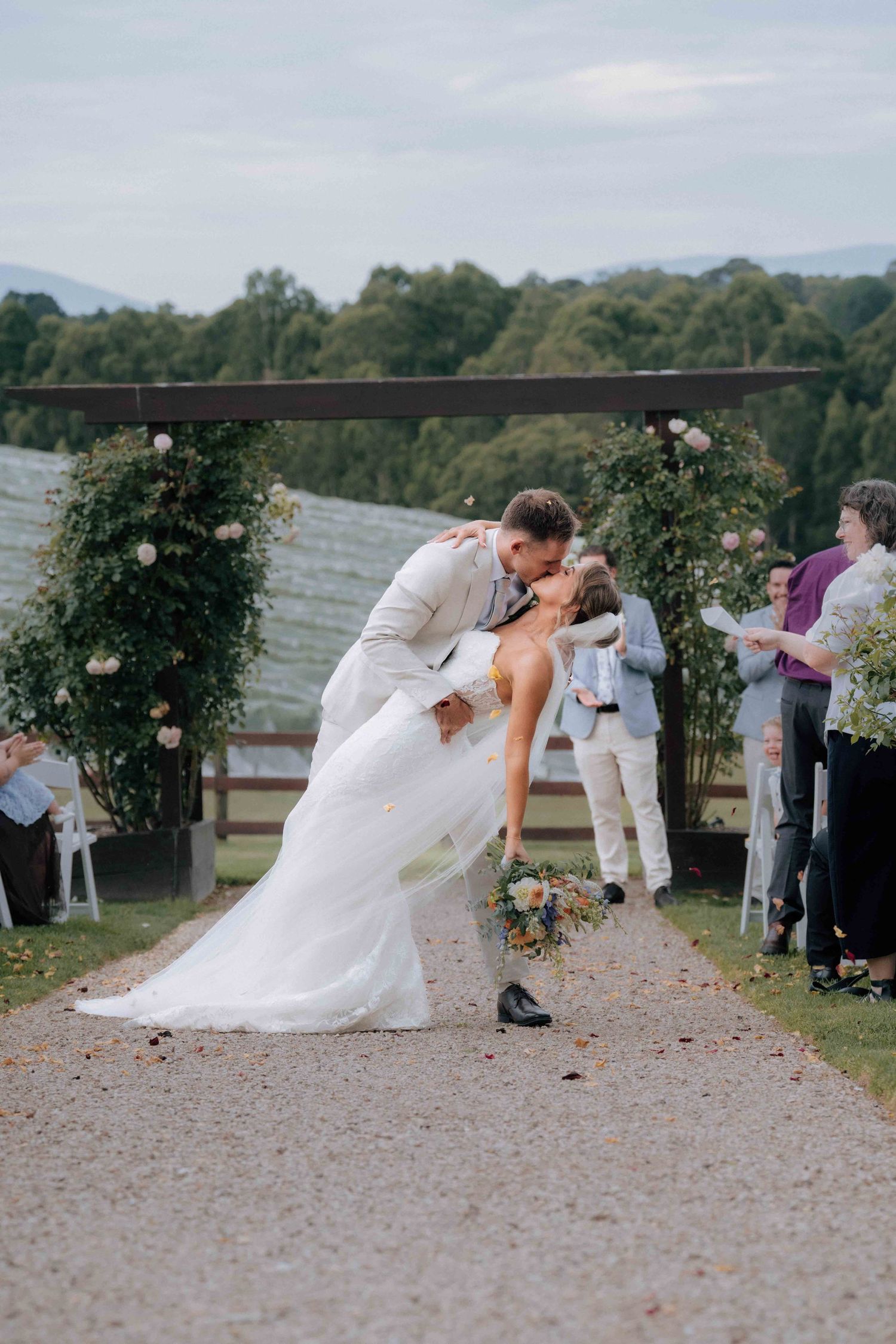 Bride and groom sharing a romantic dip kiss at outdoor wedding ceremony arch with floral decorations.