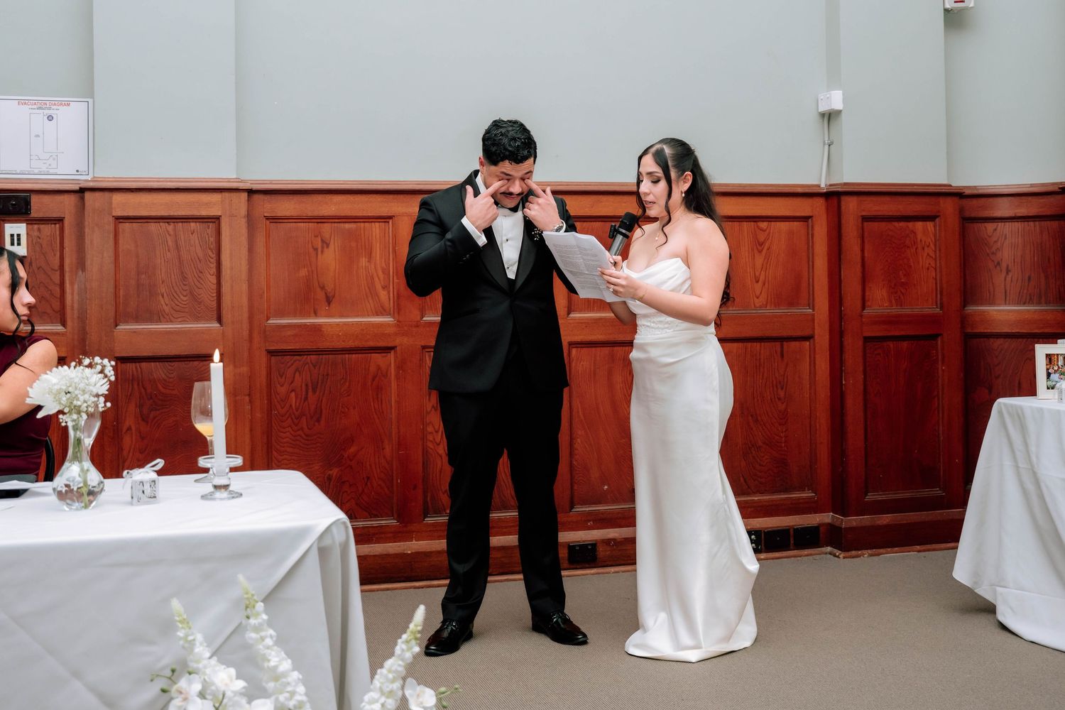 Emotional groom wipes tears as bride reads wedding vows at ceremony.