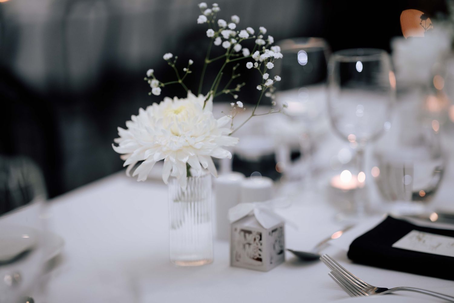 White chrysanthemum and baby's breath centerpiece in a glass vase on a white wedding reception table.
