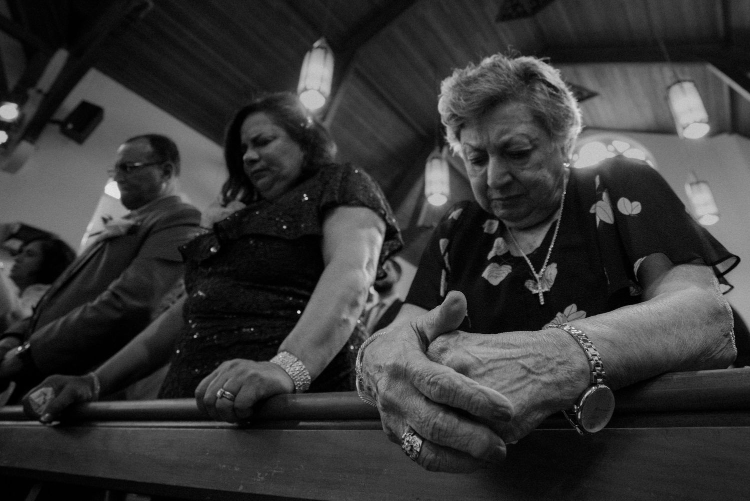 Elderly wedding guests praying in church pew in black and white photograph.