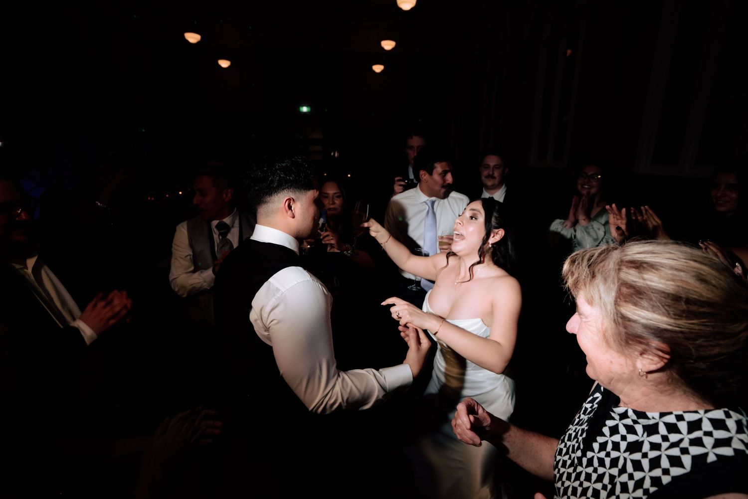 Bride and groom sharing intimate dance moment surrounded by guests at dimly lit wedding reception.