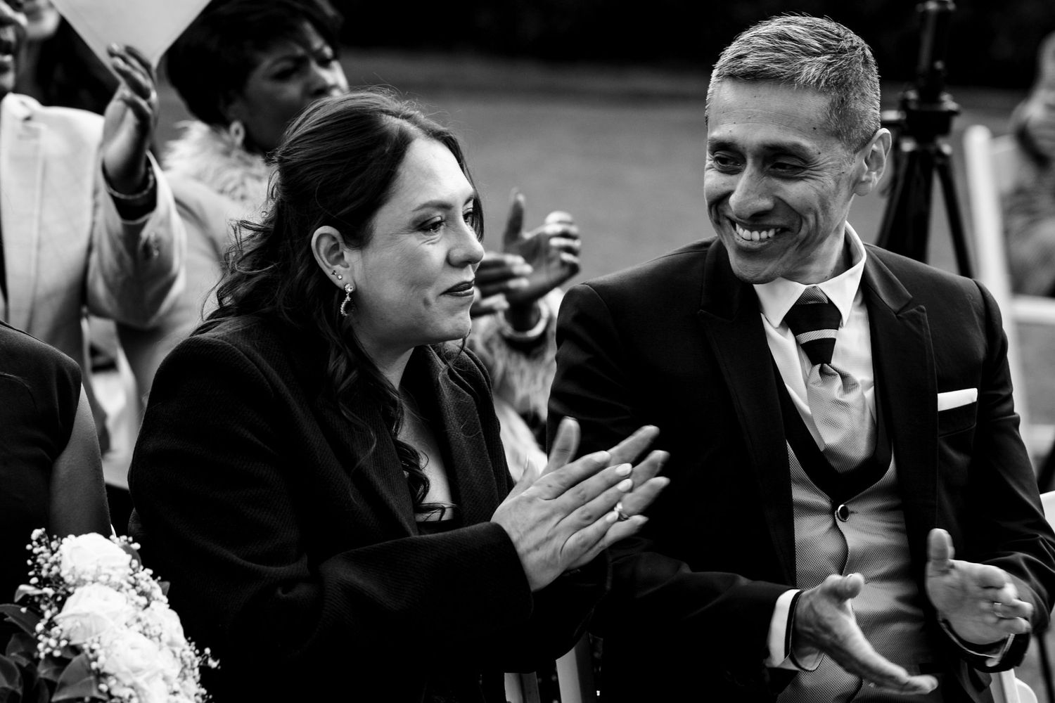 Black and white photo of two smiling wedding guests applauding during the ceremony.