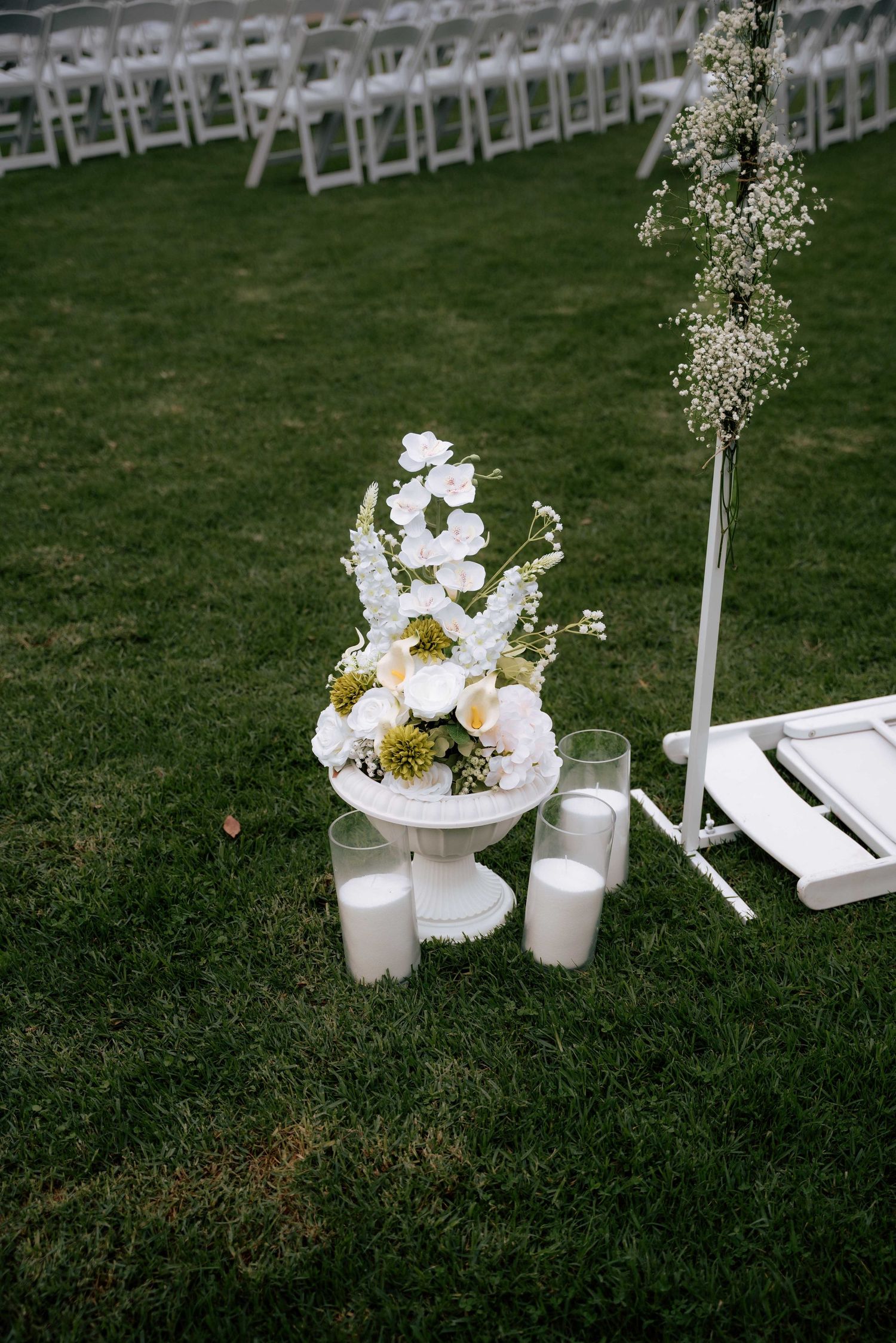 White floral wedding ceremony arrangement with candles on grass beside a decorative arch.