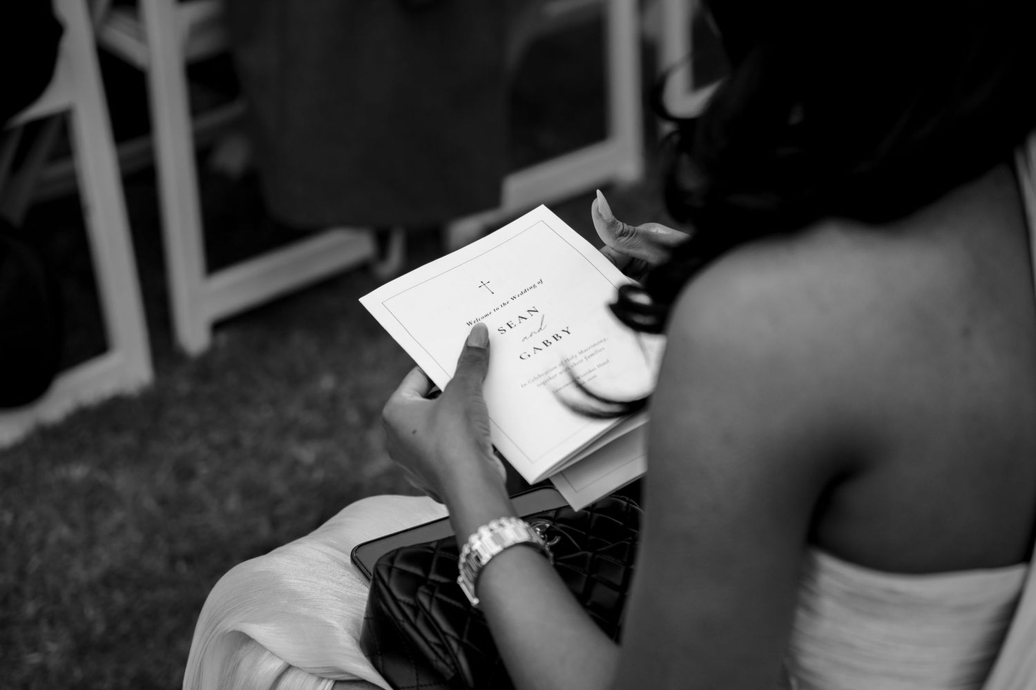 Wedding guest reading ceremony program in black and white close-up photo.