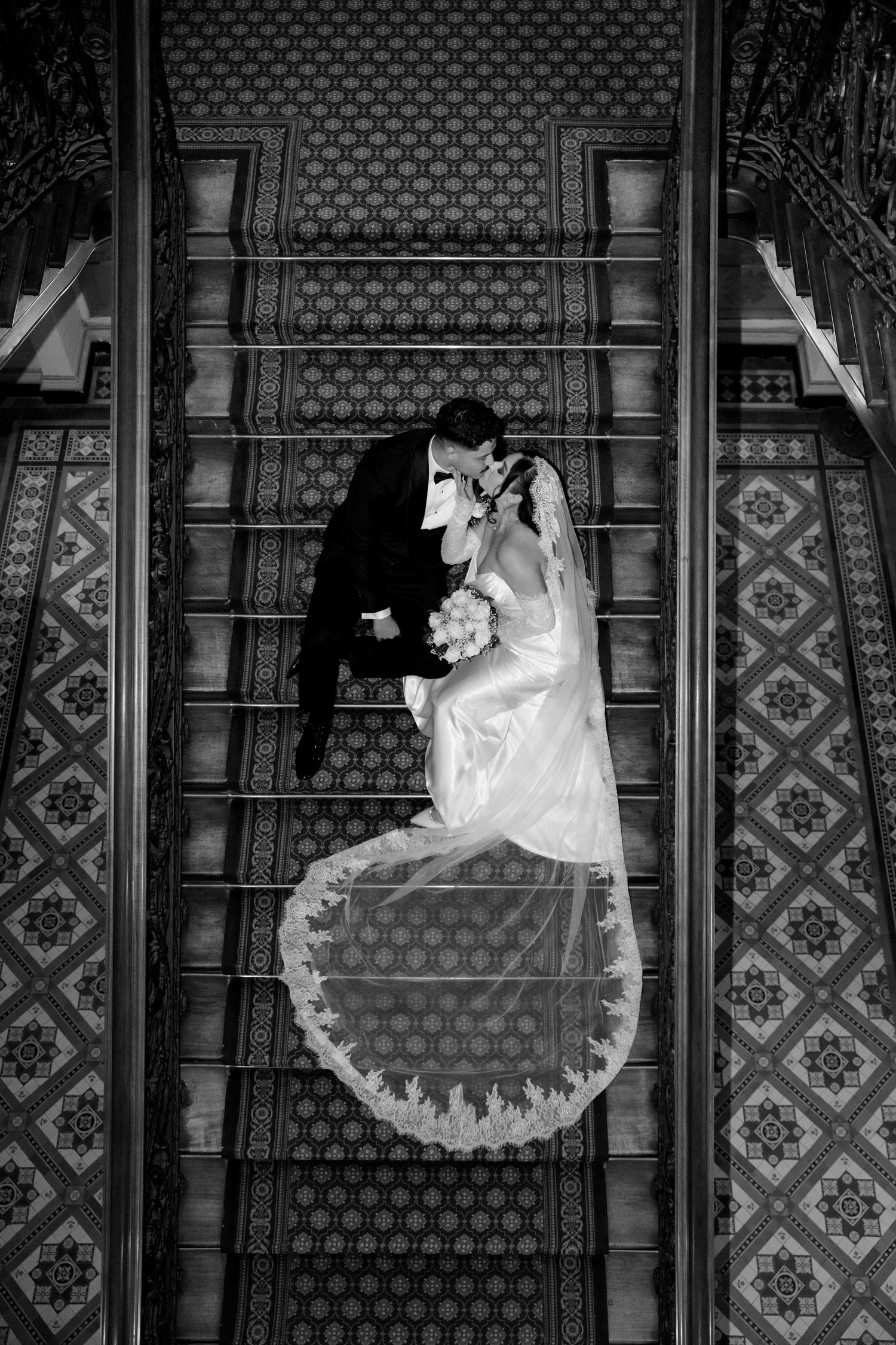 Aerial black and white photo of bride and groom kissing on grand staircase.