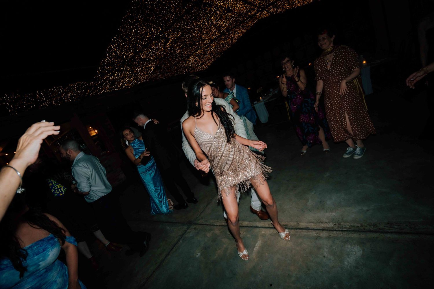 Guest in sparkly dress dances energetically on outdoor dance floor at nighttime wedding reception.