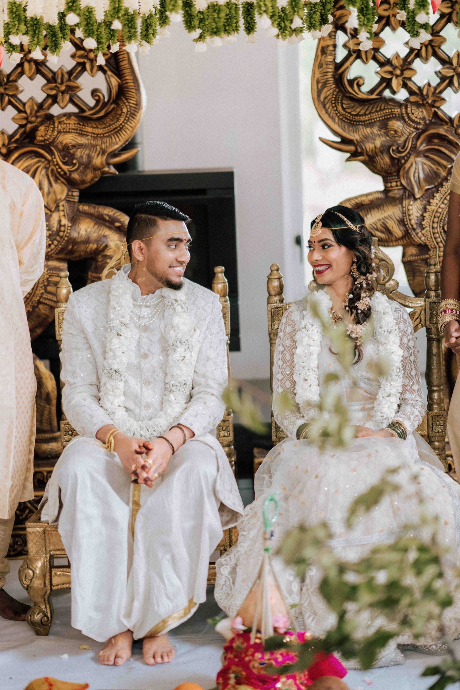 Indian bride and groom seated on ornate gold elephant thrones during traditional Hindu wedding ceremony.