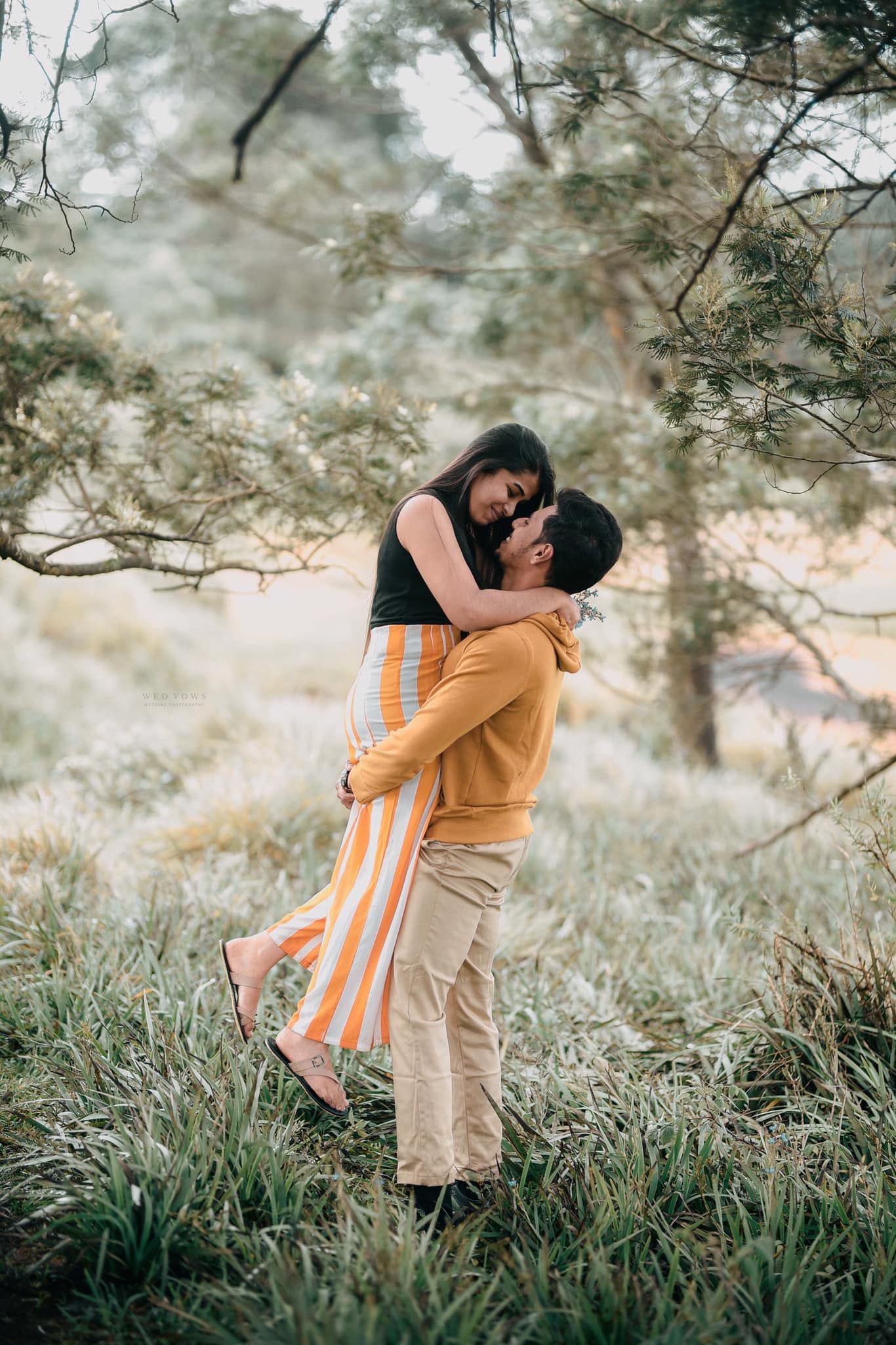 Man lifting woman in a loving embrace in a lush green forest meadow during golden hour.