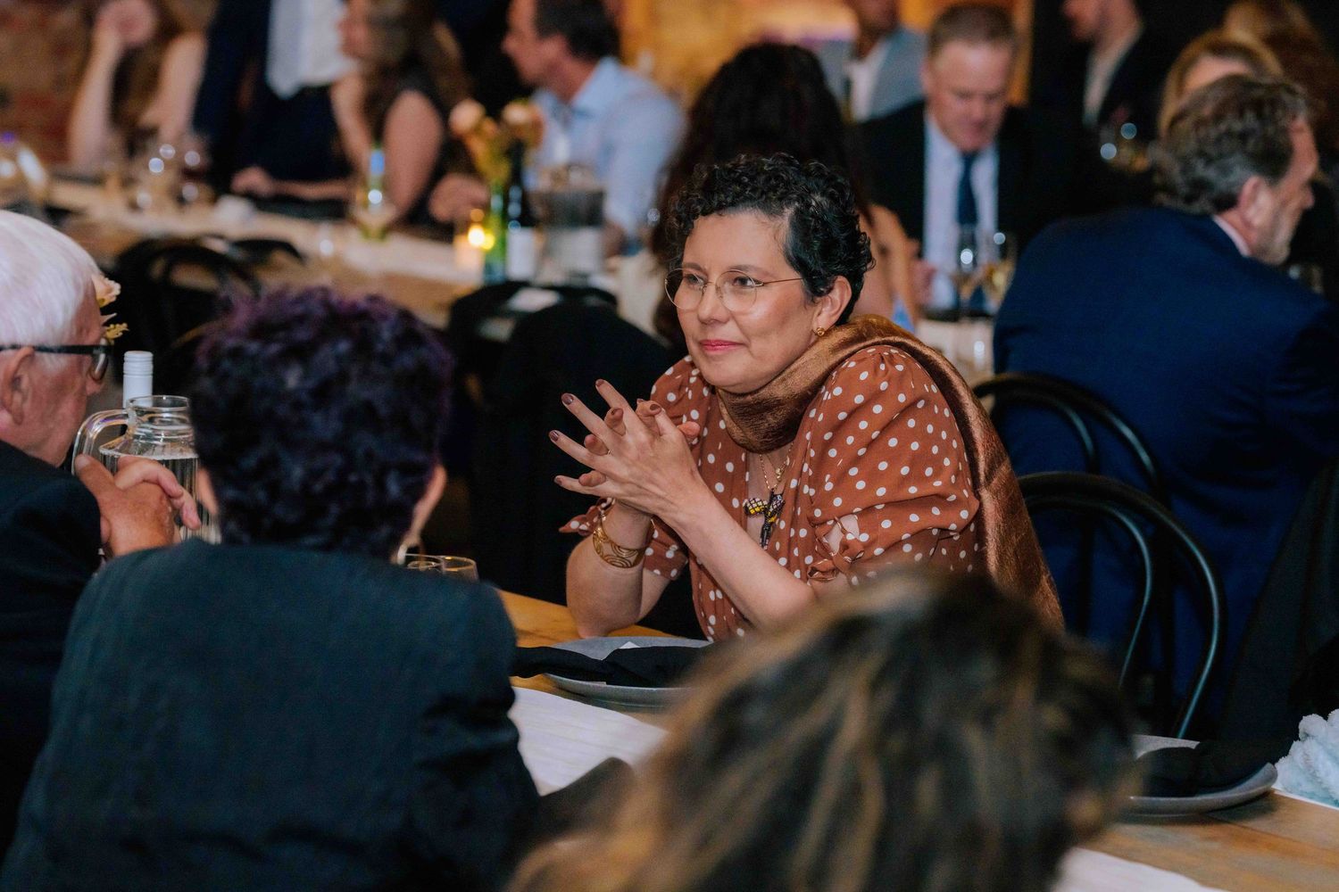 Elegant wedding guest in brown floral dress engaged in conversation at reception dinner.