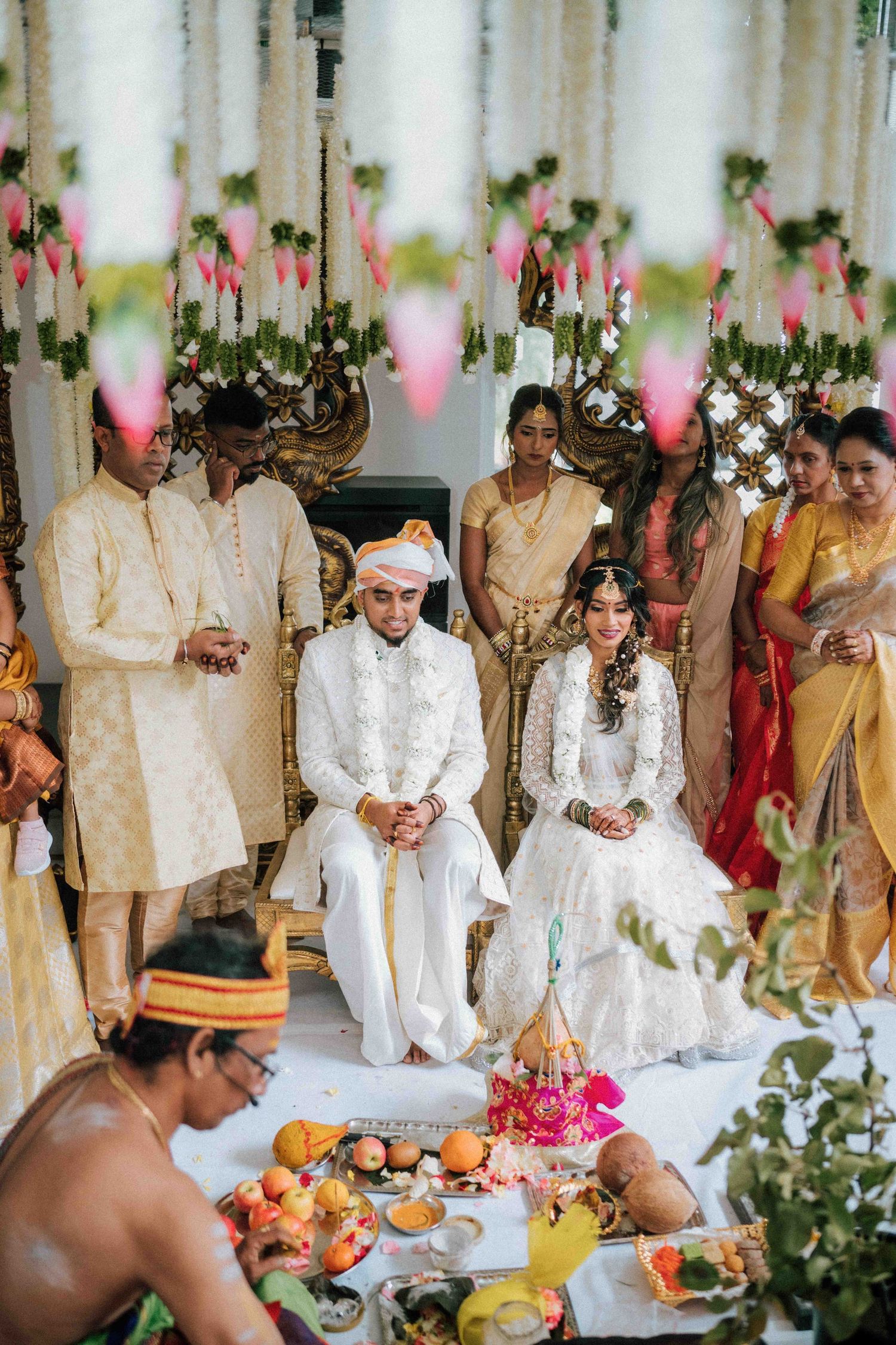 Bride and groom seated at Hindu wedding ceremony with priest and family members in traditional attire.