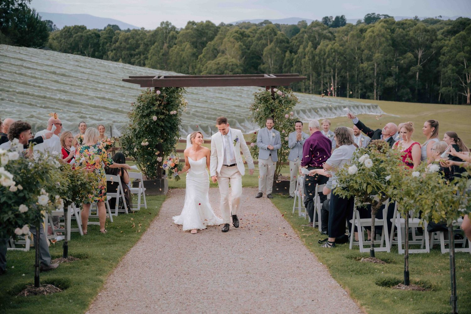 Bride and groom walk down outdoor aisle at vineyard wedding ceremony.