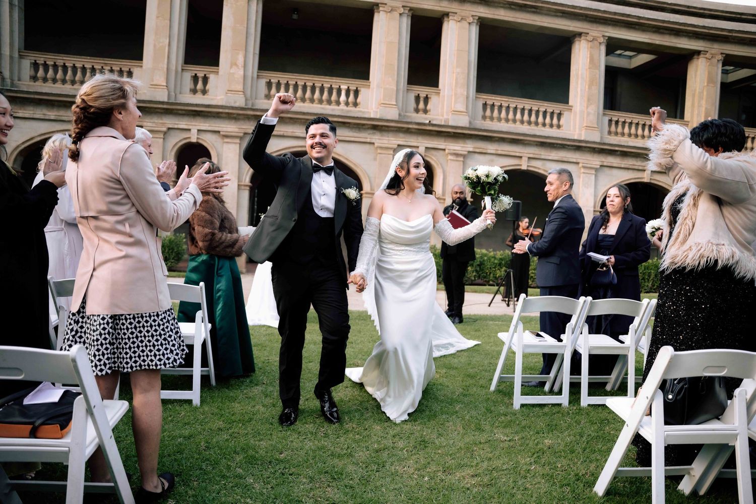 Excited bride and groom walk back down the aisle after wedding ceremony at elegant outdoor venue.
