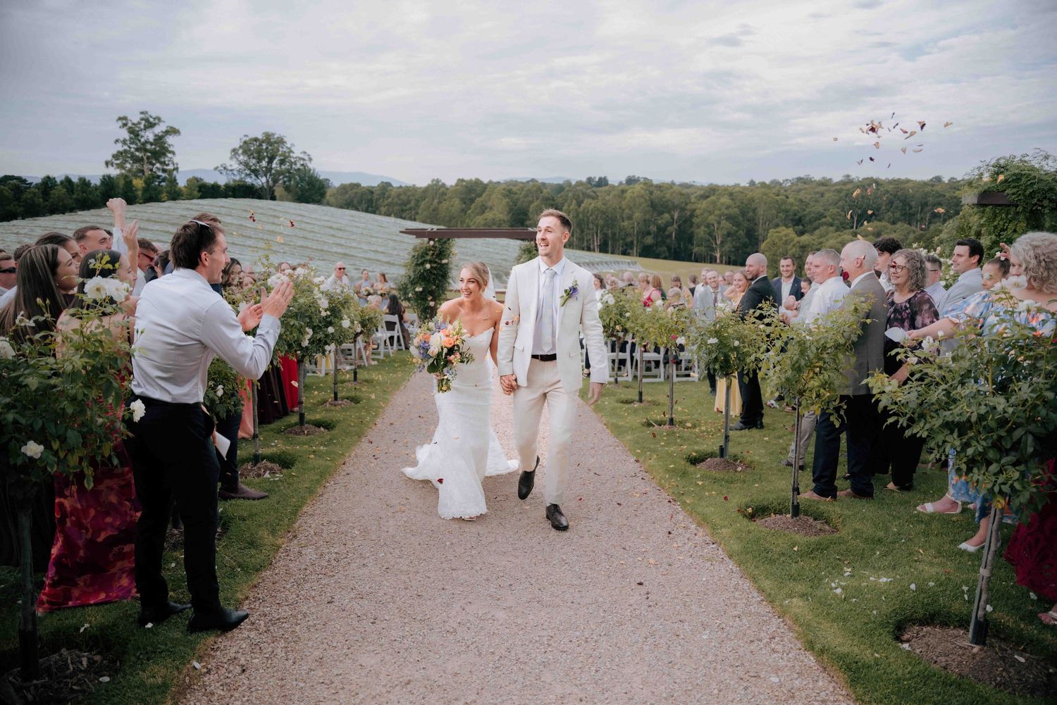 Bride and groom joyfully exit outdoor vineyard wedding ceremony with cheering guests.