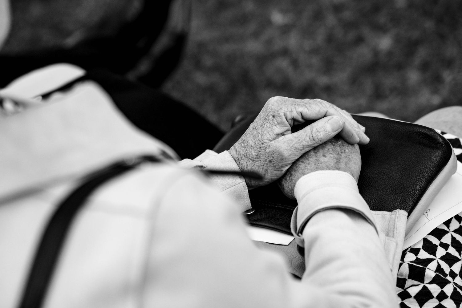 Black and white close-up of elderly hands clasped together at a wedding.