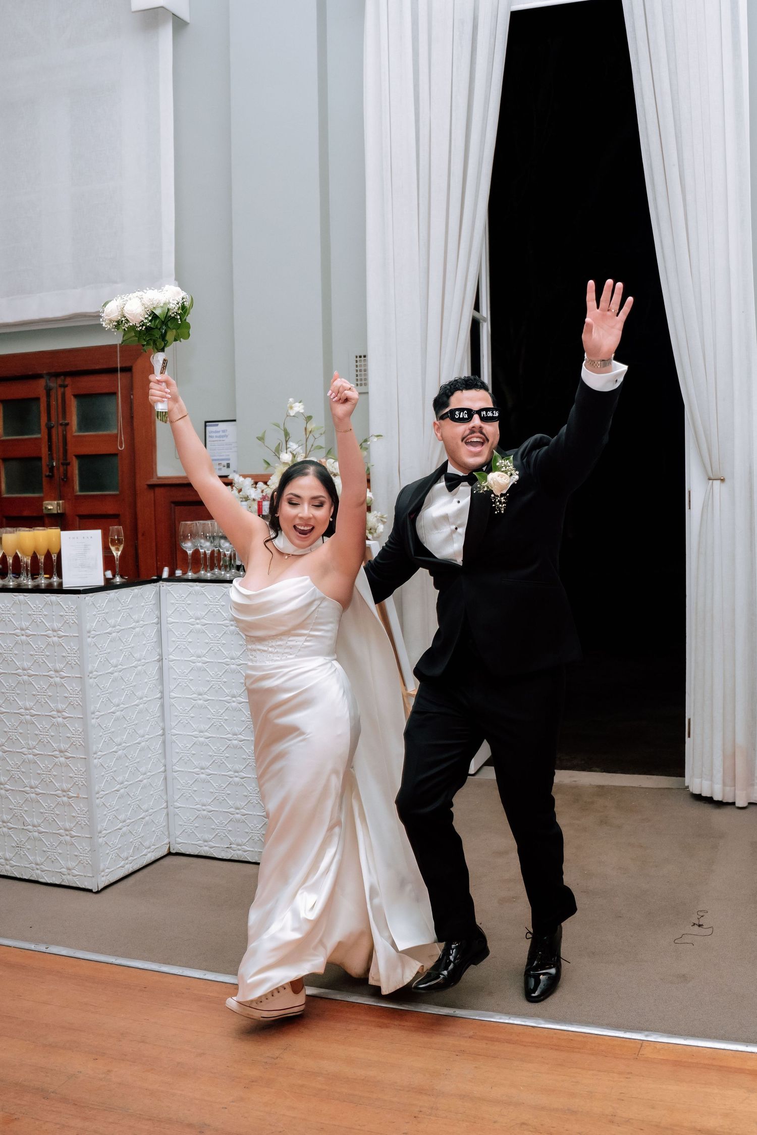 Bride and groom celebrate grand entrance at wedding reception with arms raised in excitement.
