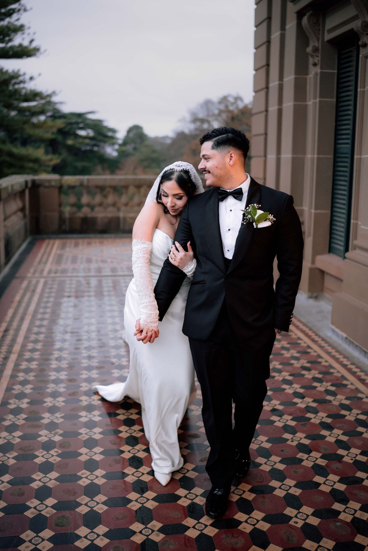 Bride and groom walk hand in hand on ornate tiled terrace at wedding venue.