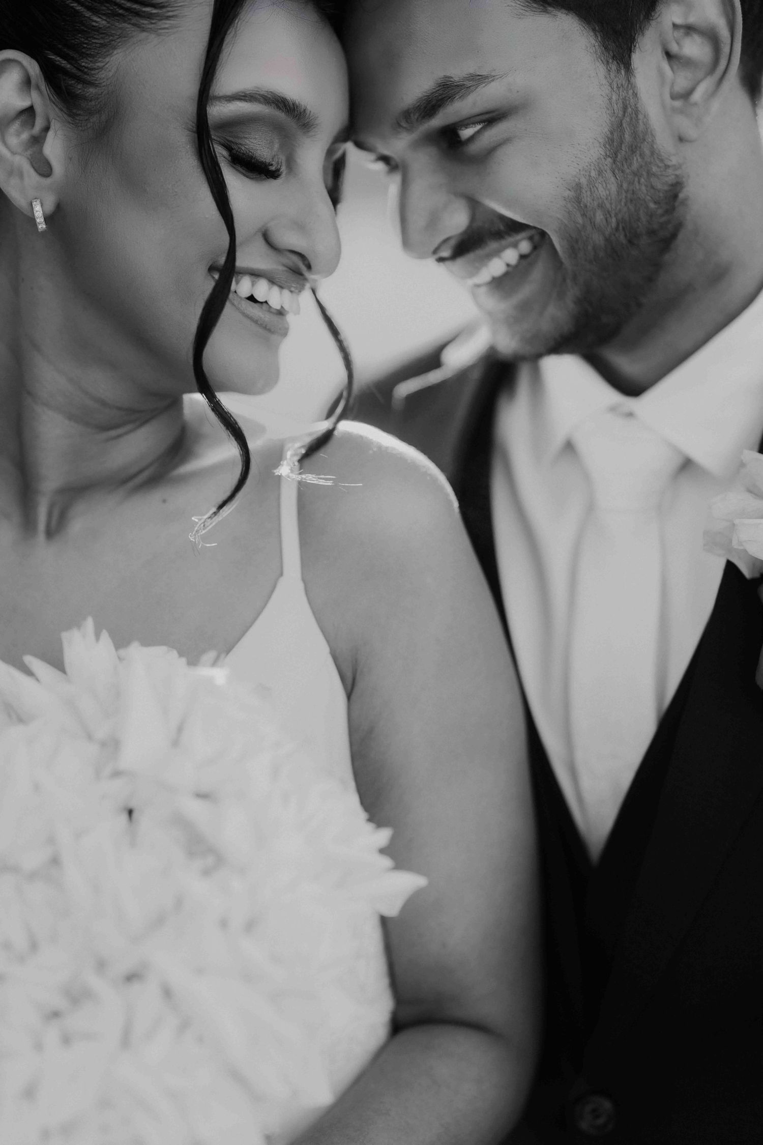Close-up black and white portrait of smiling bride and groom sharing a joyful moment together.