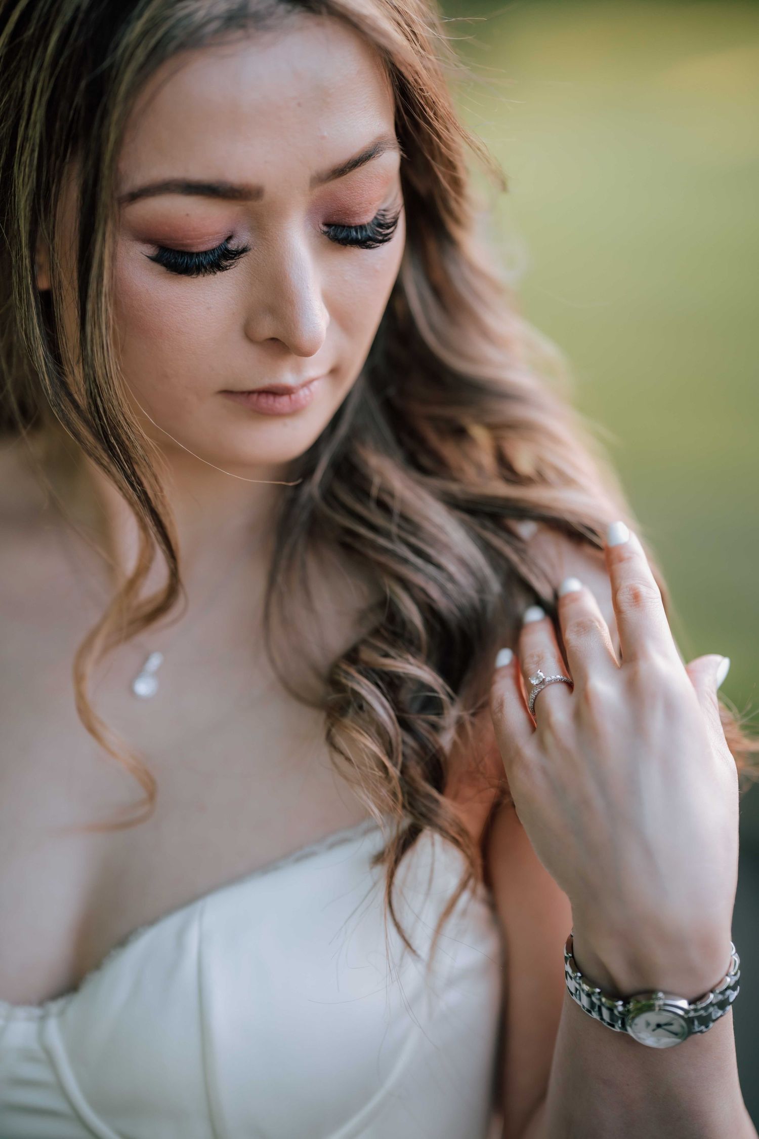 Close-up of a bride with dramatic lashes and wavy hair, showcasing her diamond engagement ring and silver watch.
