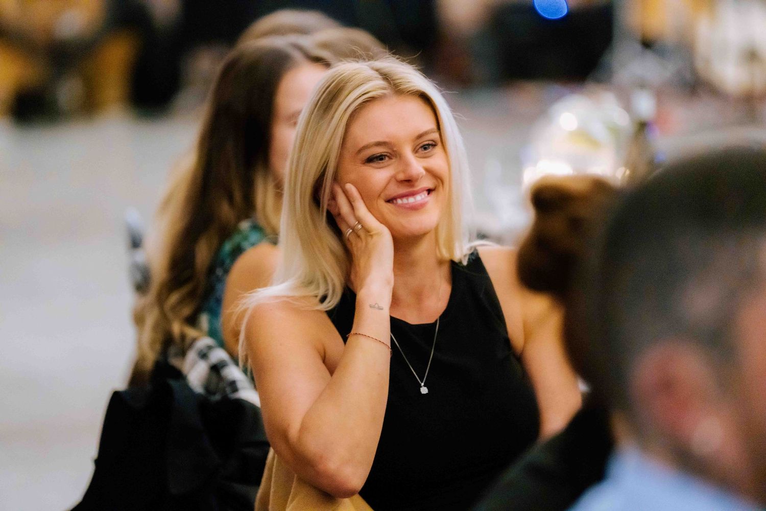 Blonde woman in black dress smiling warmly at a wedding reception event.