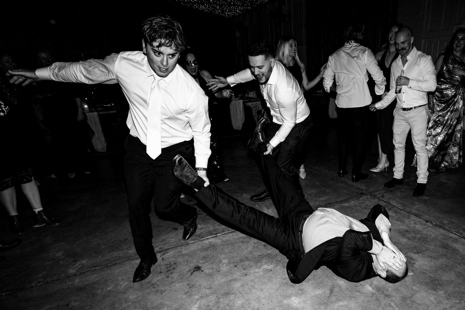 Groomsmen dancing energetically on wedding reception dance floor in black and white photo.