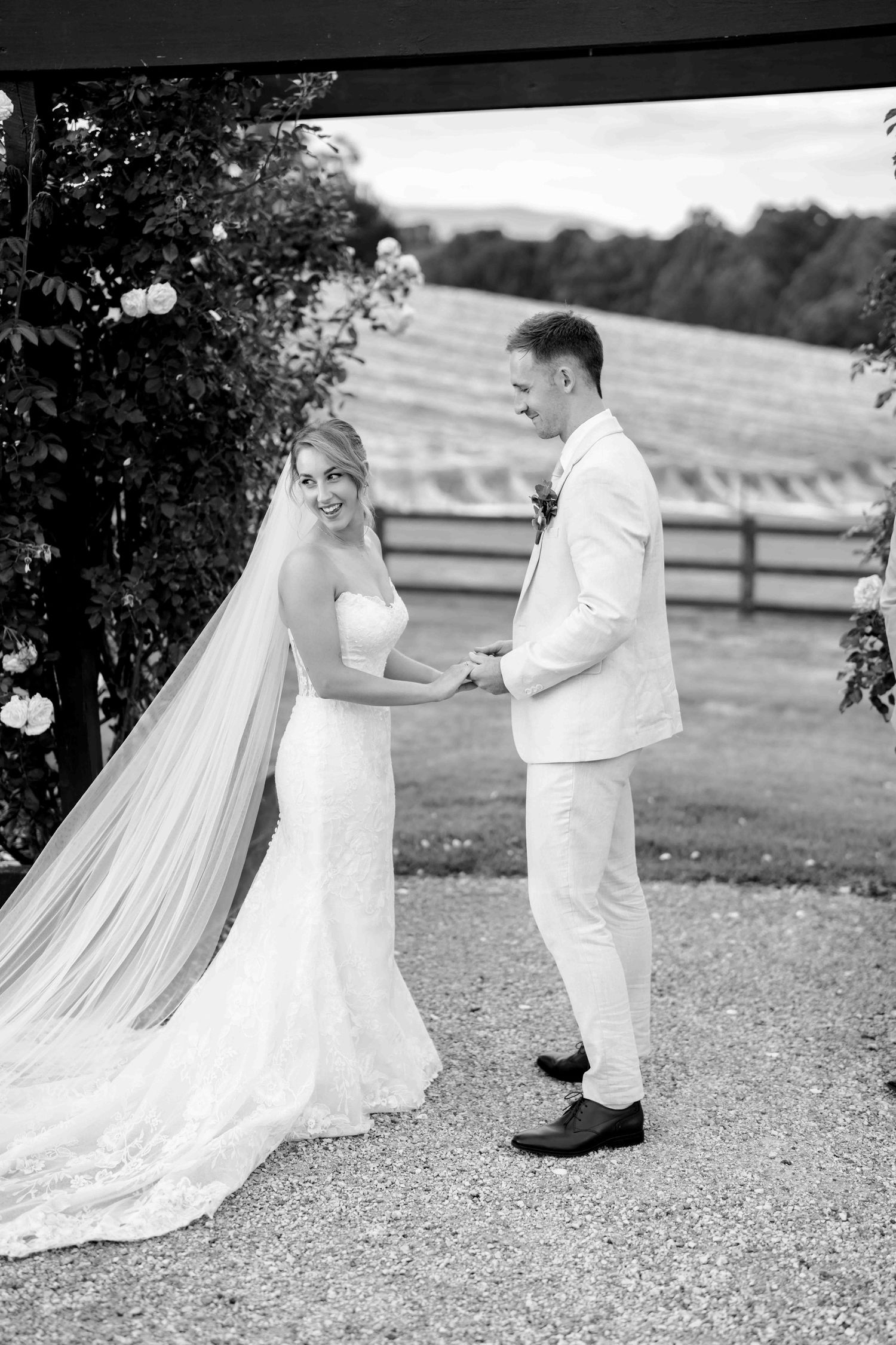 Bride and groom hold hands at floral arch in elegant black and white wedding portrait outdoors.