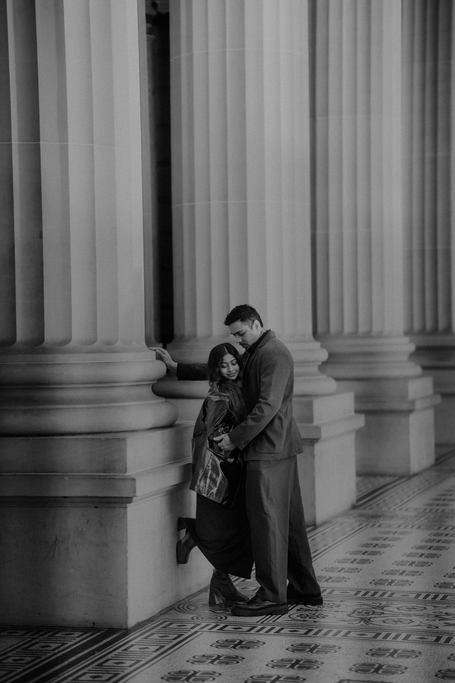 Black and white romantic photo of couple embracing against tall stone columns.