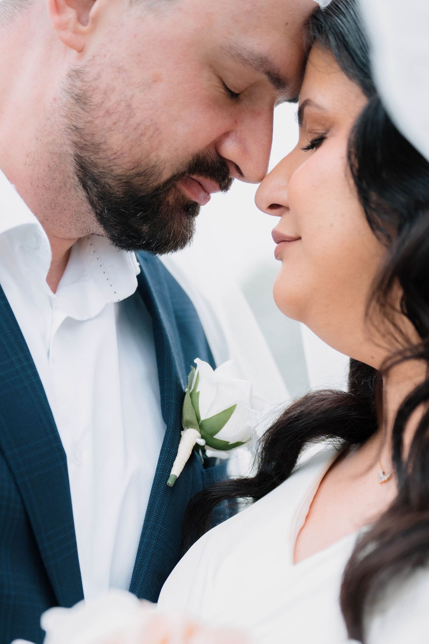 Close-up portrait of bride and groom touching foreheads with eyes closed in a romantic wedding moment.
