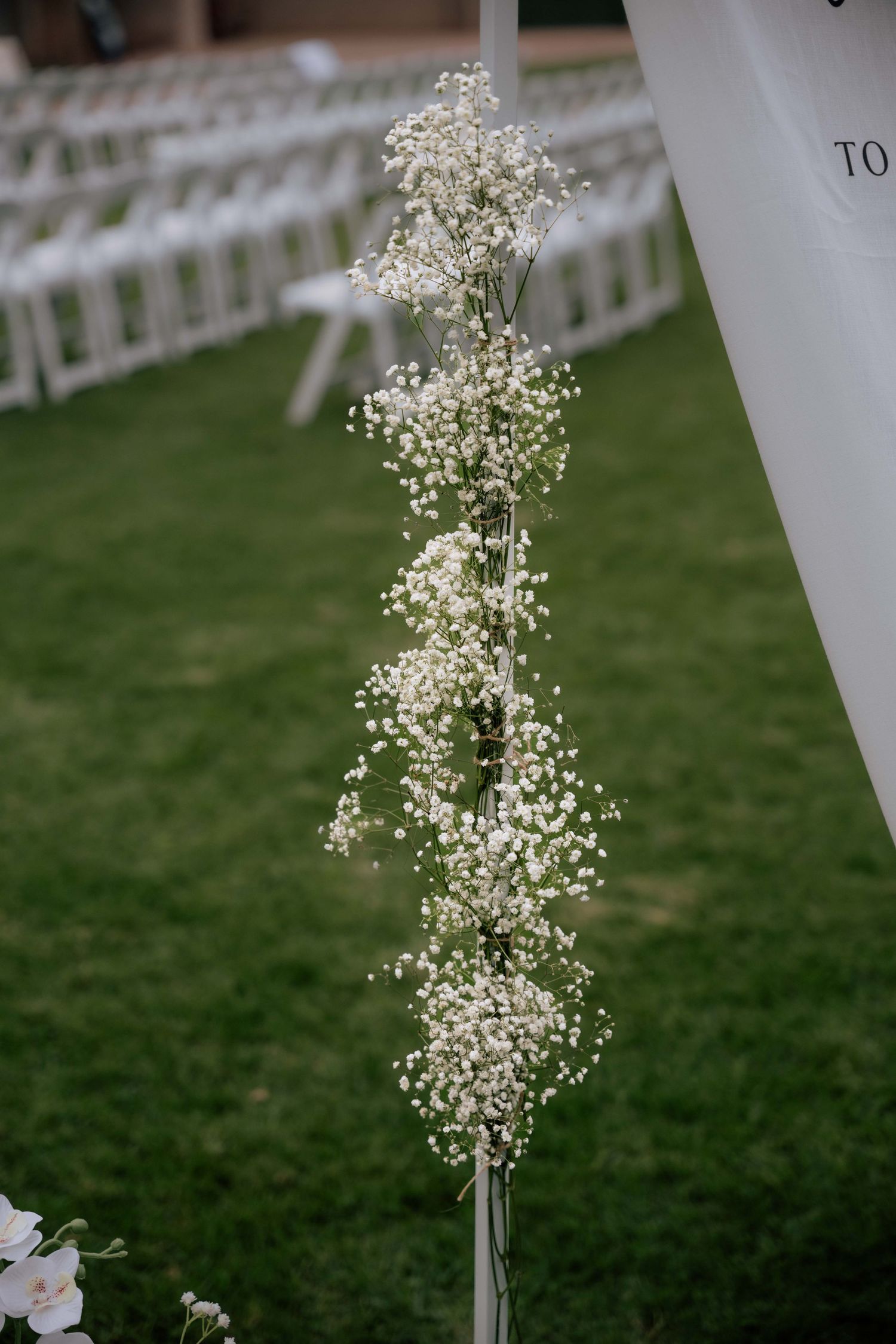 Delicate white baby's breath floral garland decorating wedding ceremony arch outdoors.