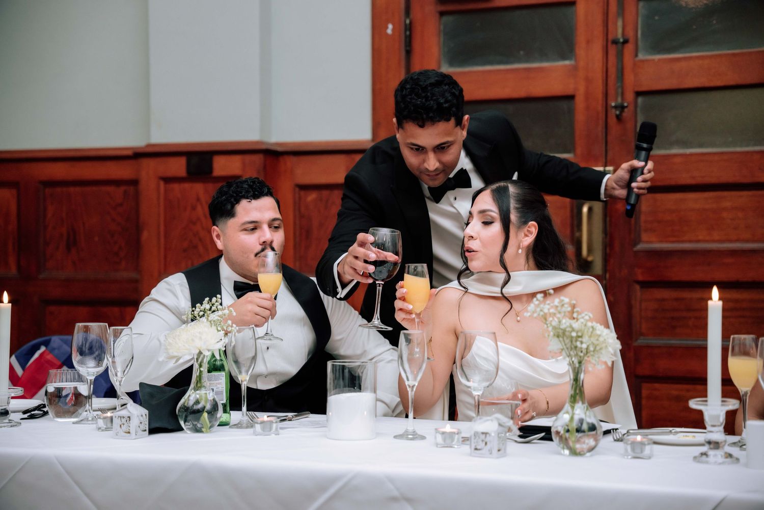 Bride and groom toast with champagne at wedding reception head table with candles and florals.