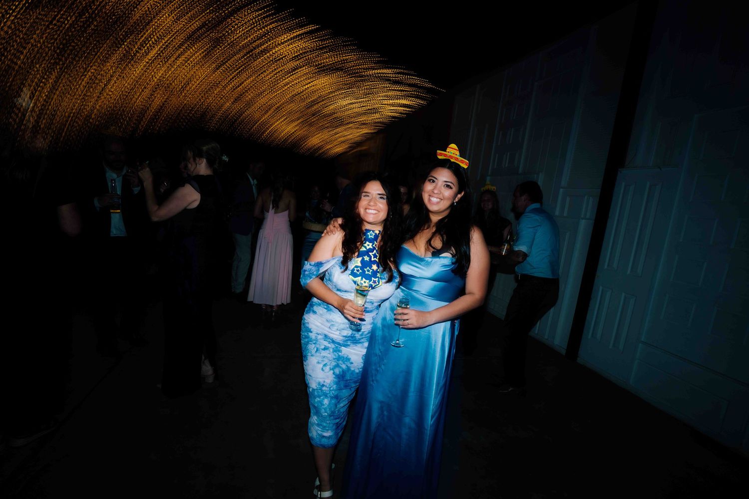 Two women in blue formal dresses pose together at a dimly lit prom or formal event.