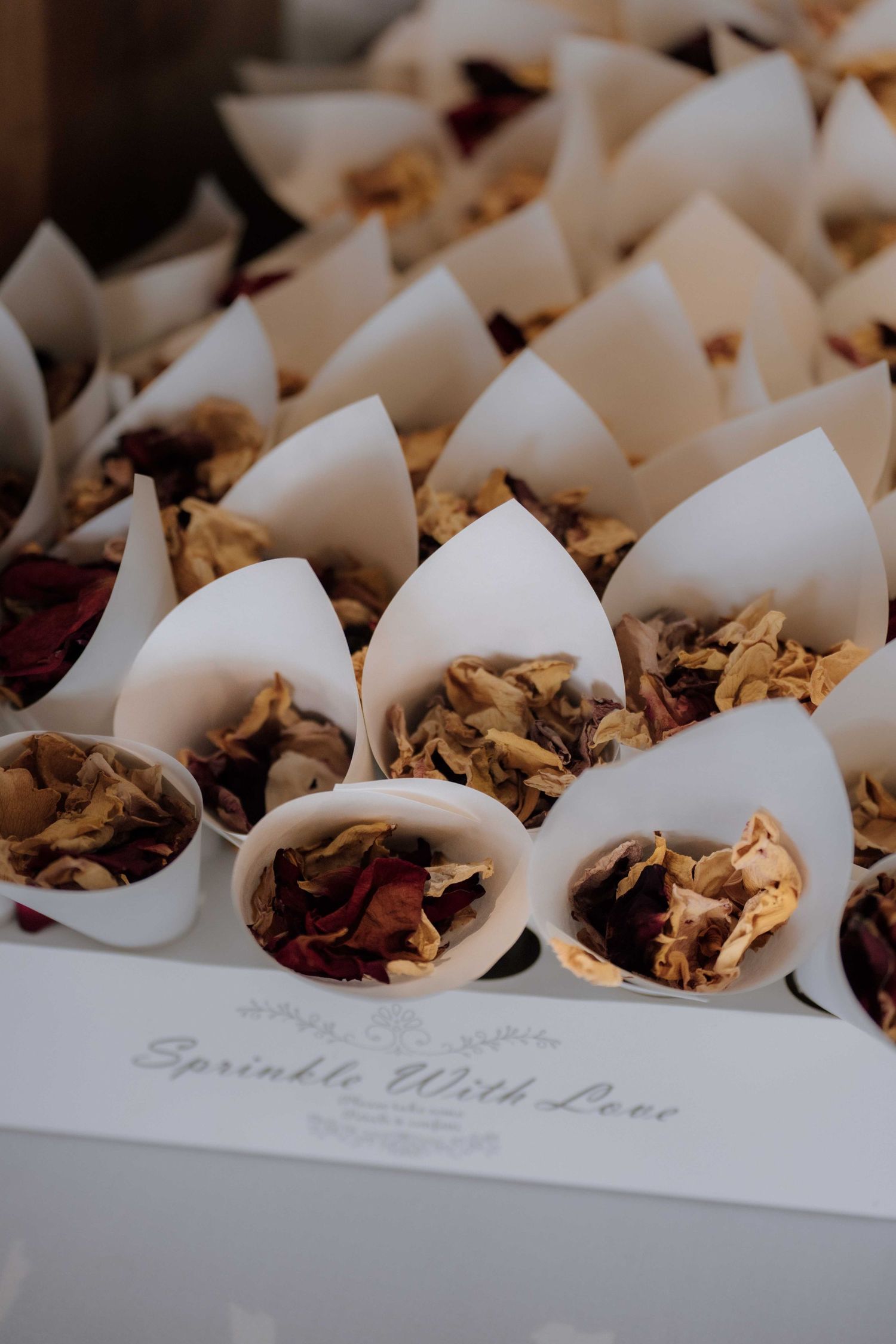 White paper cones filled with dried flower petals in a box labeled Sprinkle With Love for a wedding.