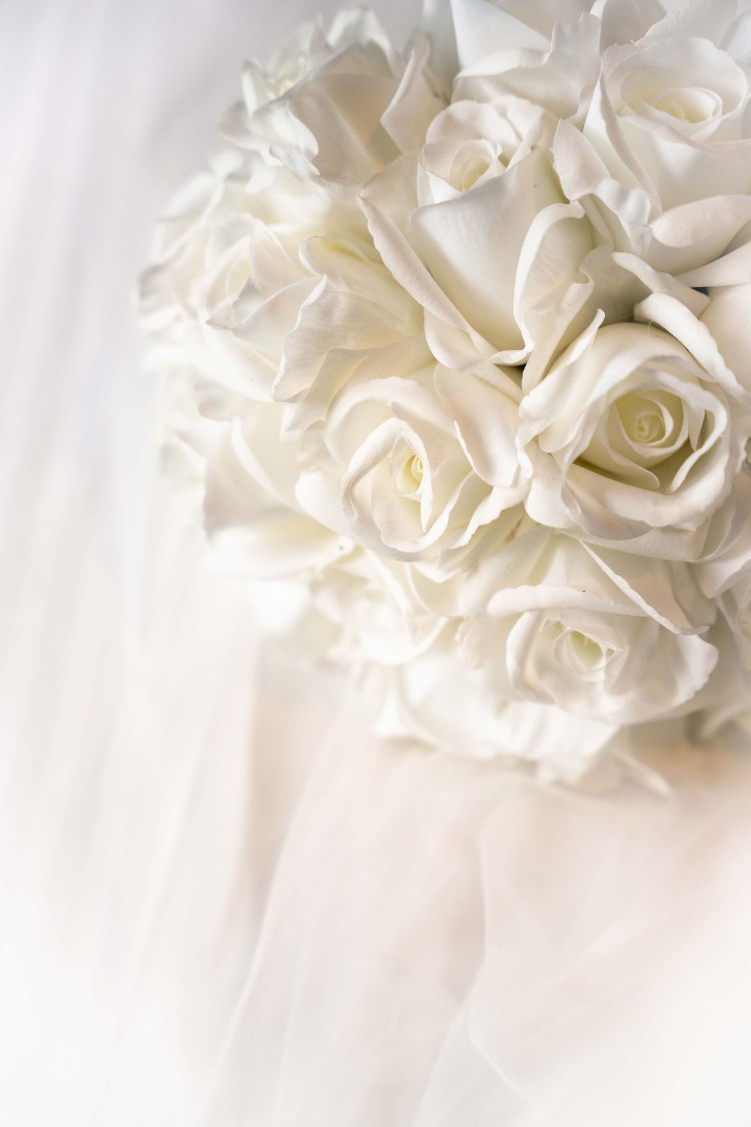 Elegant white rose bridal bouquet resting on soft white wedding veil.
