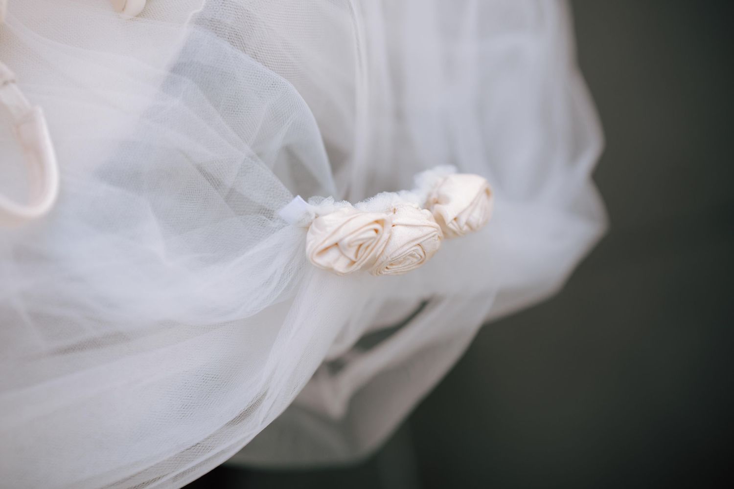 Close-up of white tulle wedding veil adorned with delicate fabric rose embellishments.