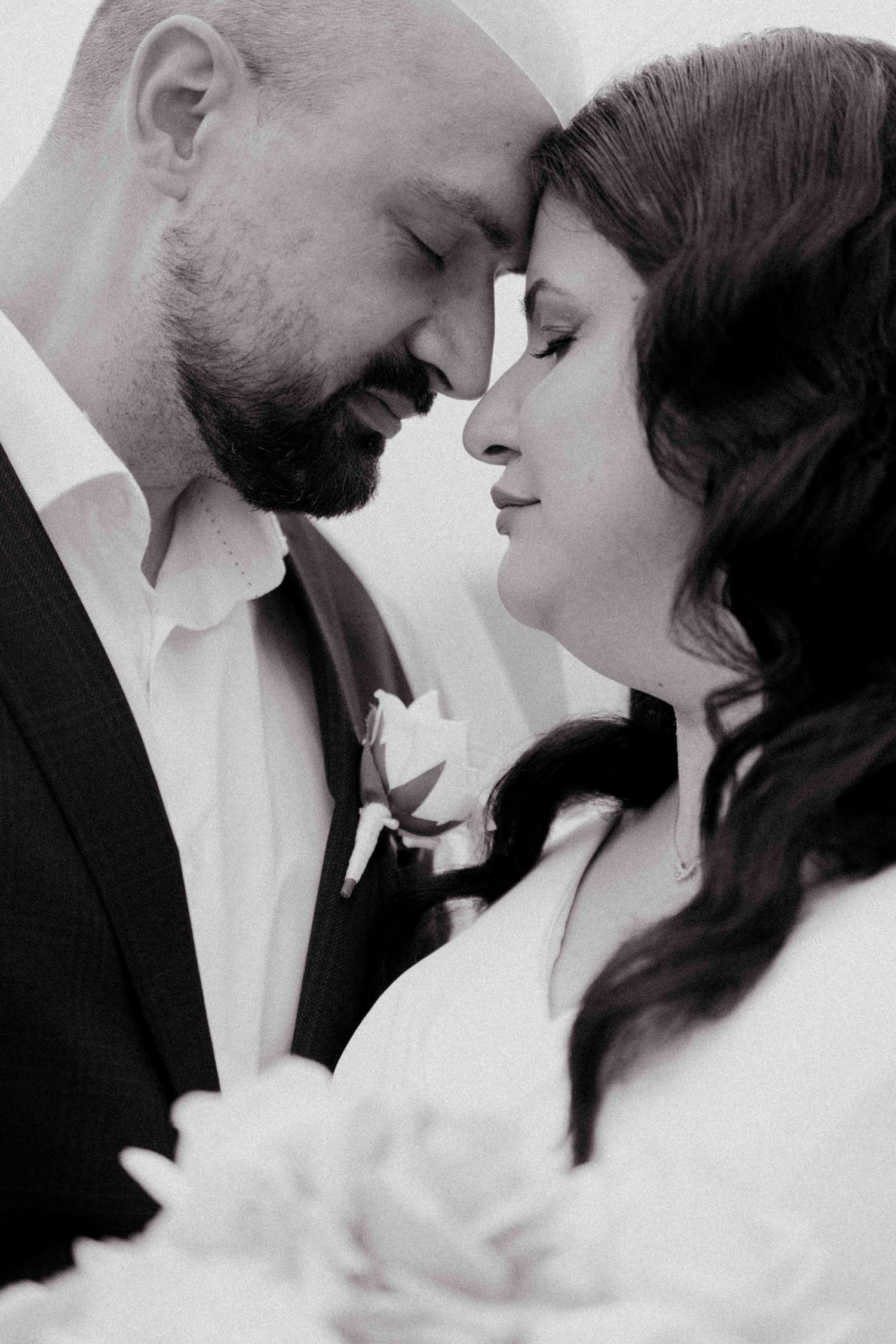 Black and white portrait of bride and groom touching foreheads in a tender romantic moment.