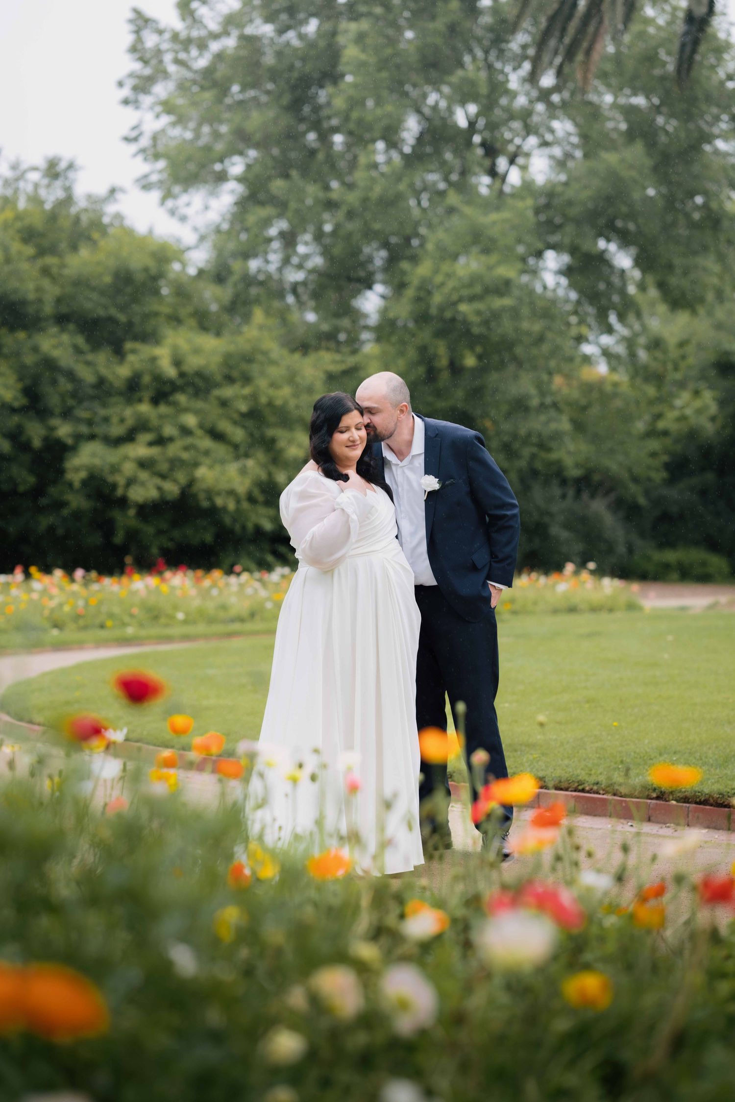 Bride and groom share a tender moment surrounded by vibrant colorful flowers in a beautiful garden setting.