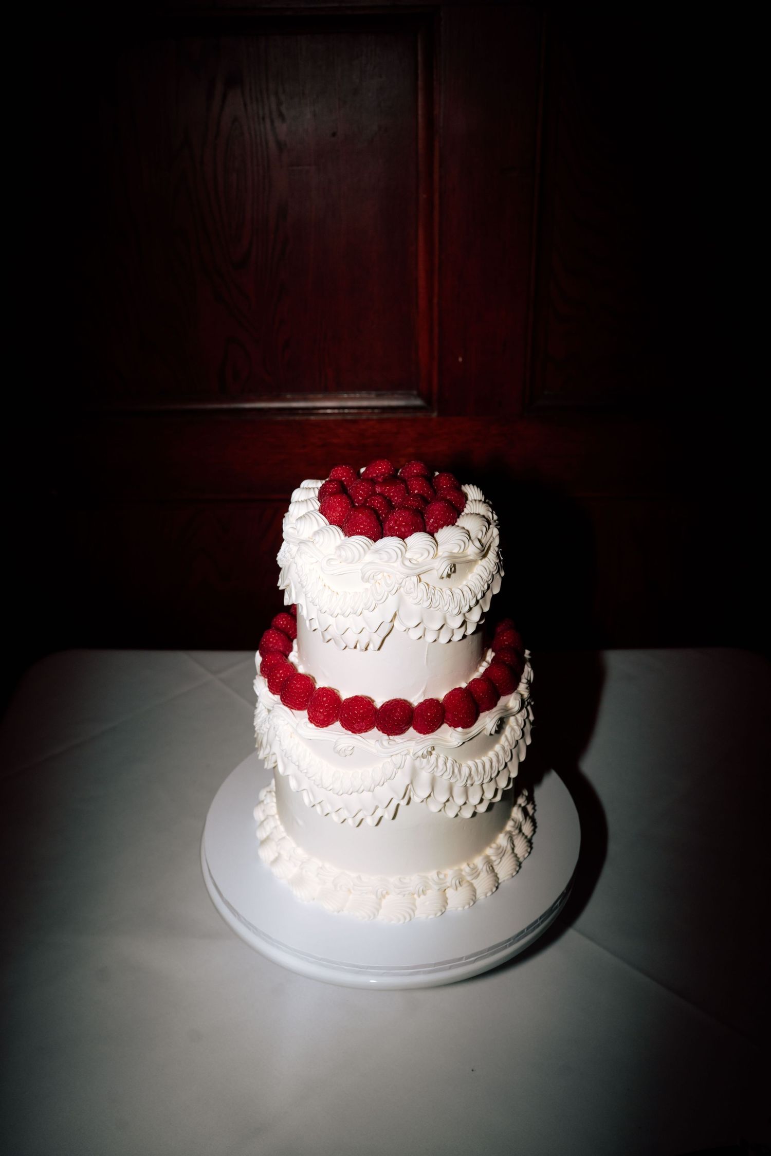 Two-tier white wedding cake decorated with red raspberries on white stand.