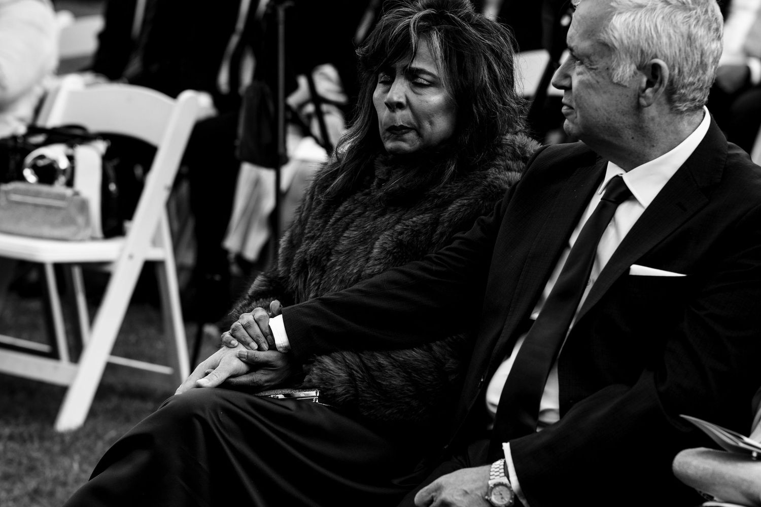 Elderly couple sitting together as wedding guests during outdoor ceremony in black and white.