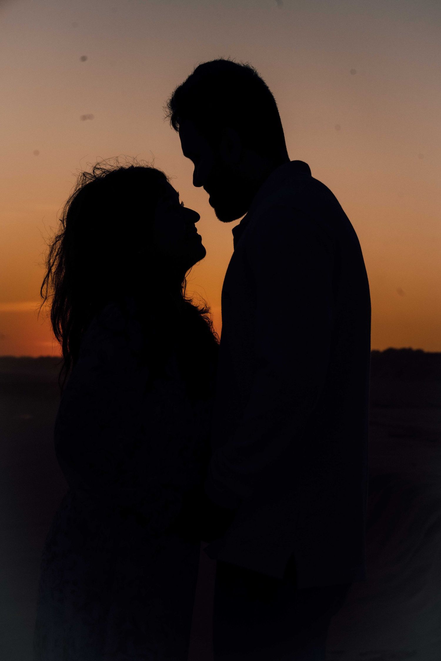 Silhouette of romantic couple facing each other against vibrant orange sunset sky on beach.