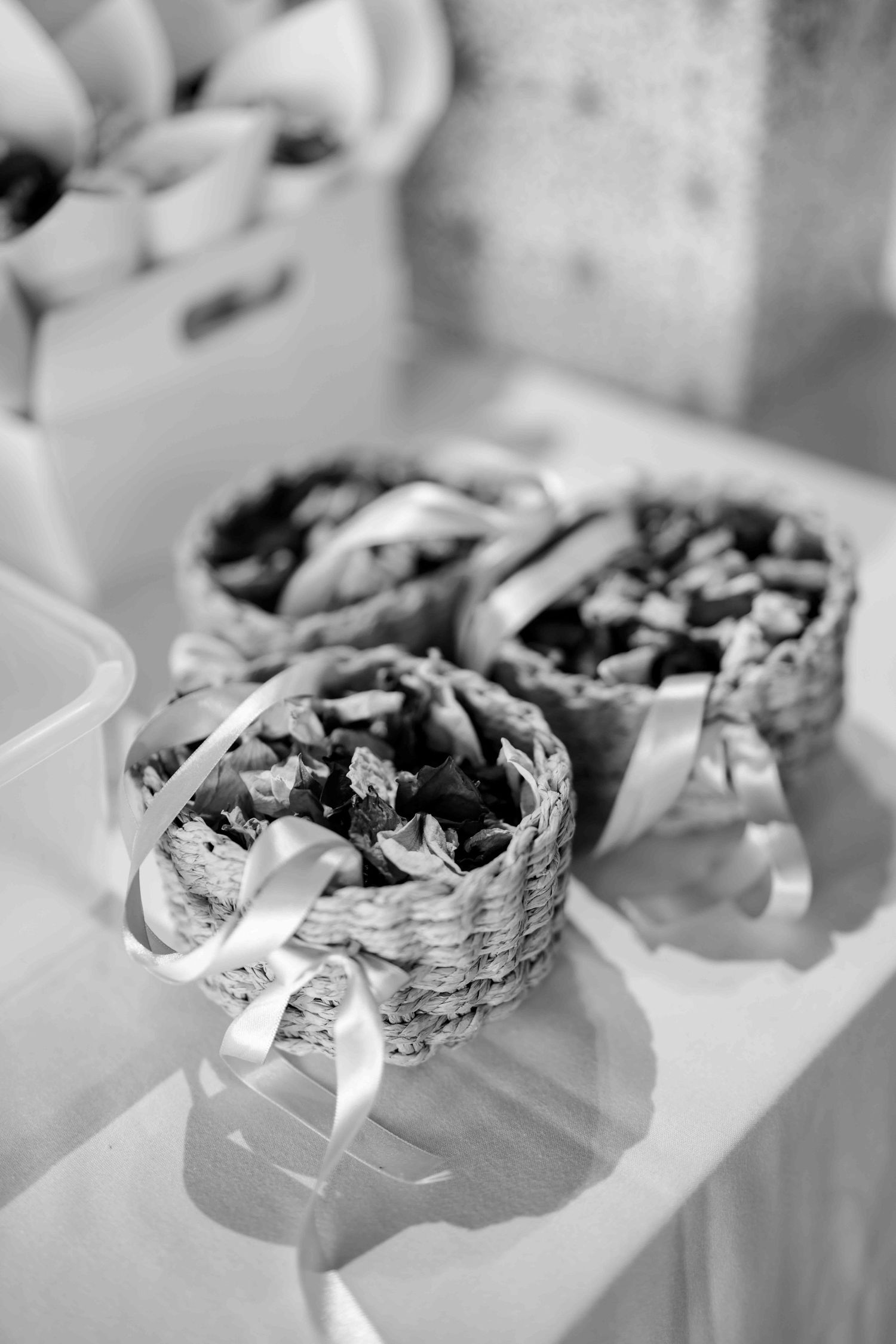 Black and white photo of wicker baskets filled with confetti and tied with white ribbons on a table.