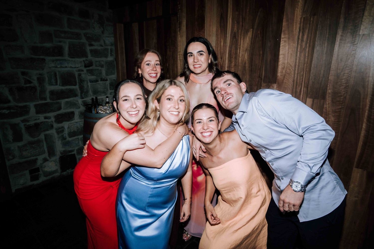 Group of six smiling wedding guests posing together for fun photo at reception.